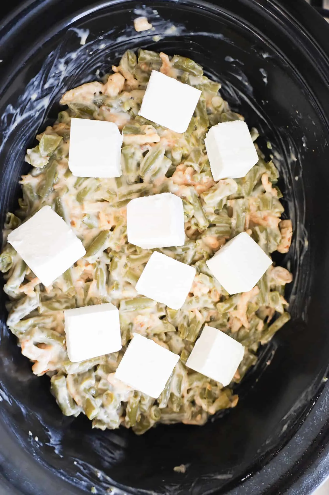 cream cheese cubes on top of green bean mixture in a crock pot