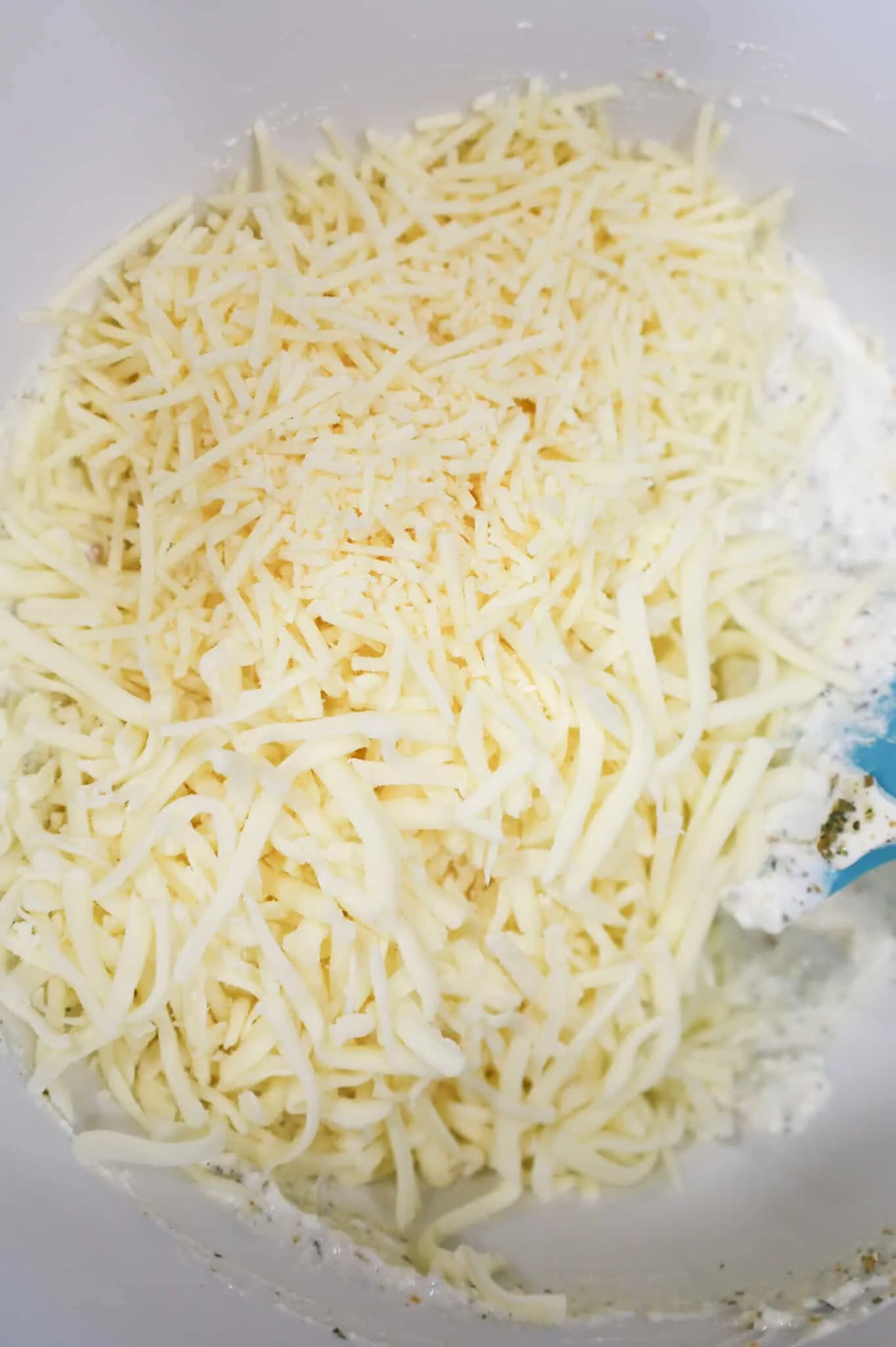 shredded mozzarella and parmesan on top of ricotta mixture in a mixing bowl