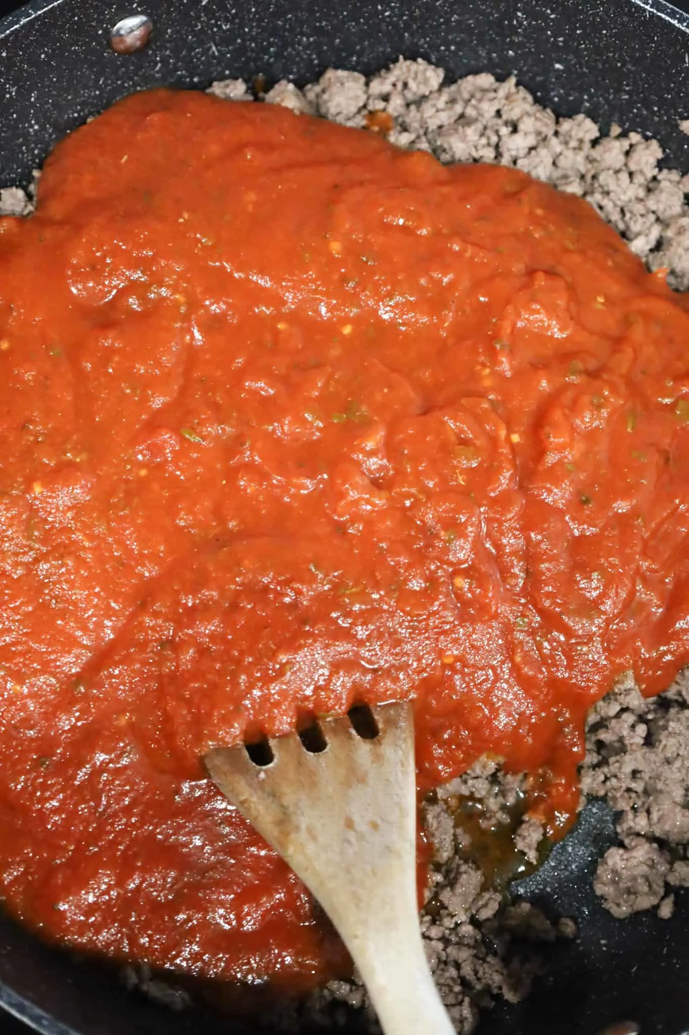 marinara on top of browned ground beef in a saute pan