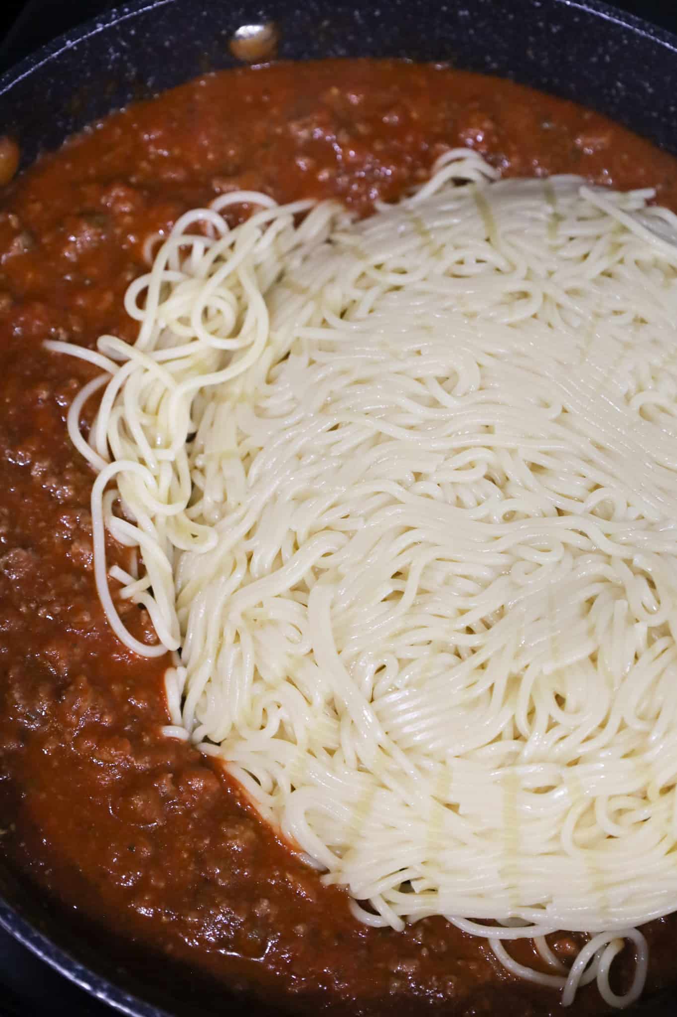 cooked spaghetti on top of marinara and ground beef in a saute pan