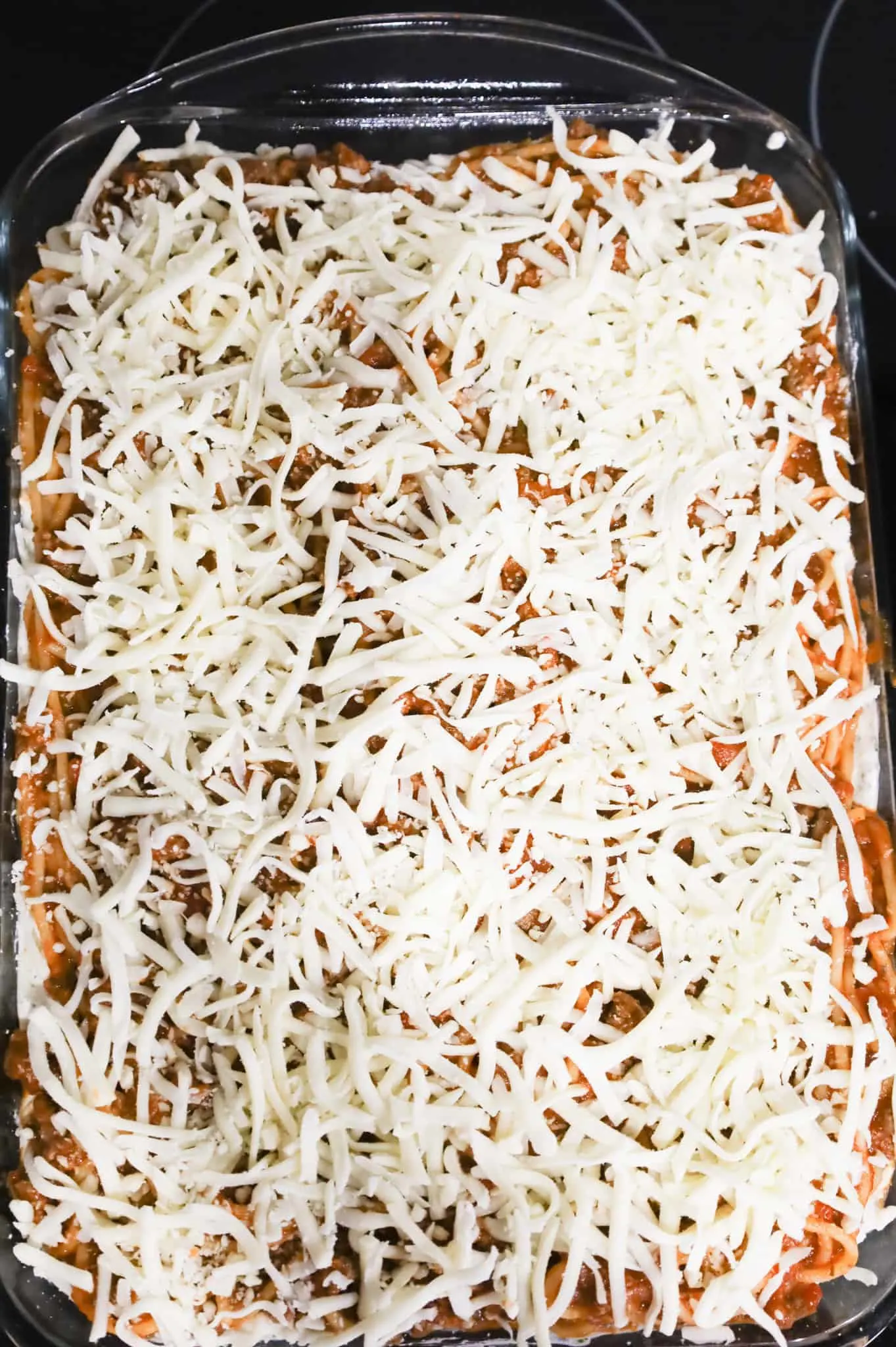 shredded mozzarella on top of spaghetti in a baking dish