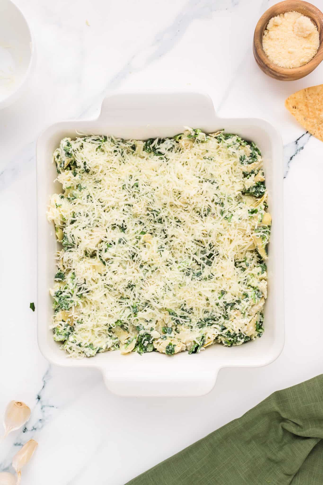 shredded mozzarella cheese on top of creamy spinach and artichoke mixture in a baking dish