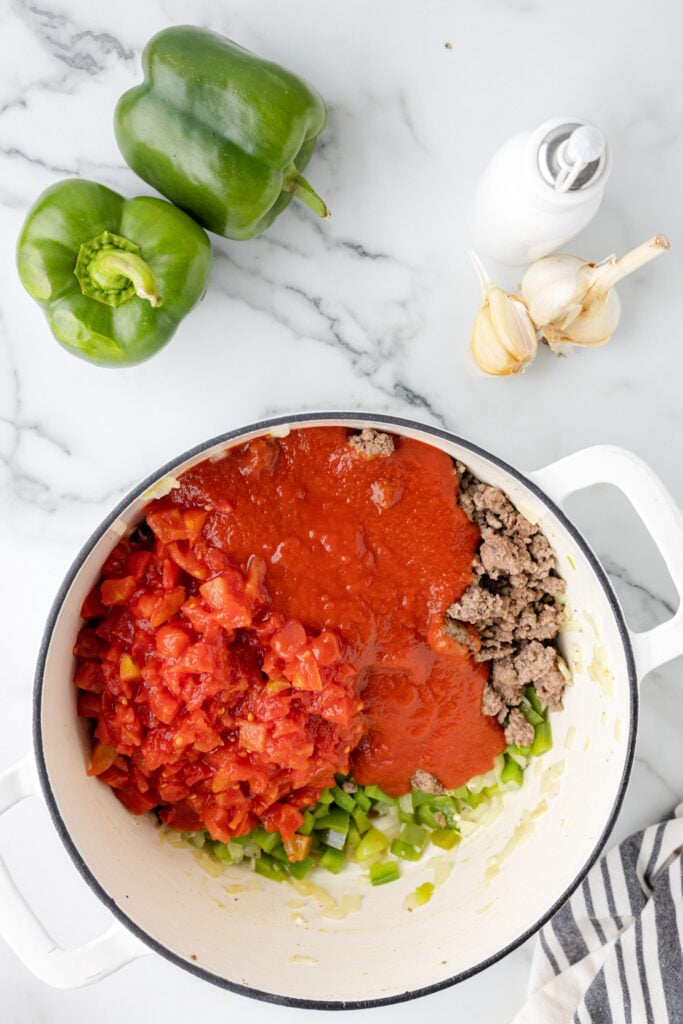diced tomatoes and tomato sauce on top of cooked ground beef and diced peppers
