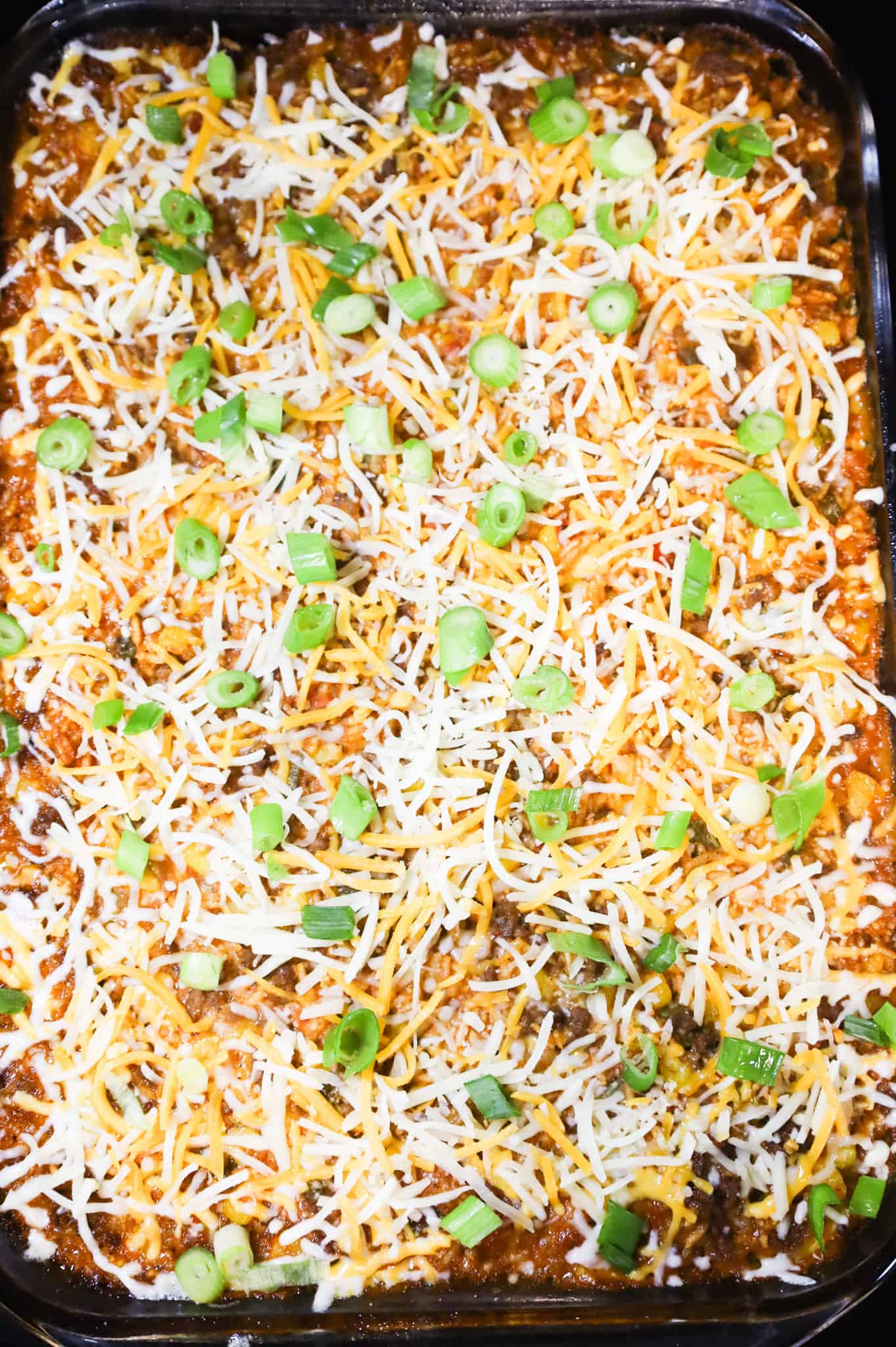 chopped green onions and shredded cheese on top of taco rice casserole