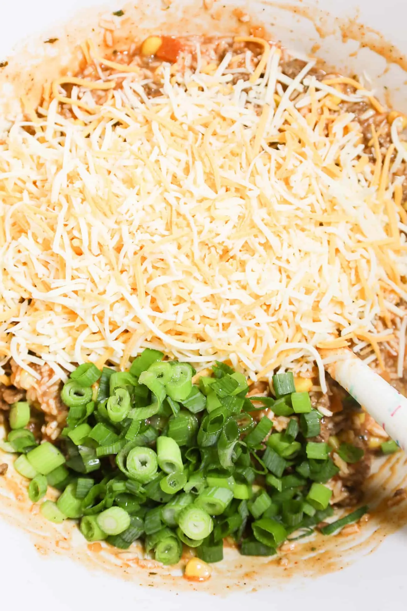 chopped green onions and shredded cheese on top of ground beef, rice and salsa mixture in a mixing bowl