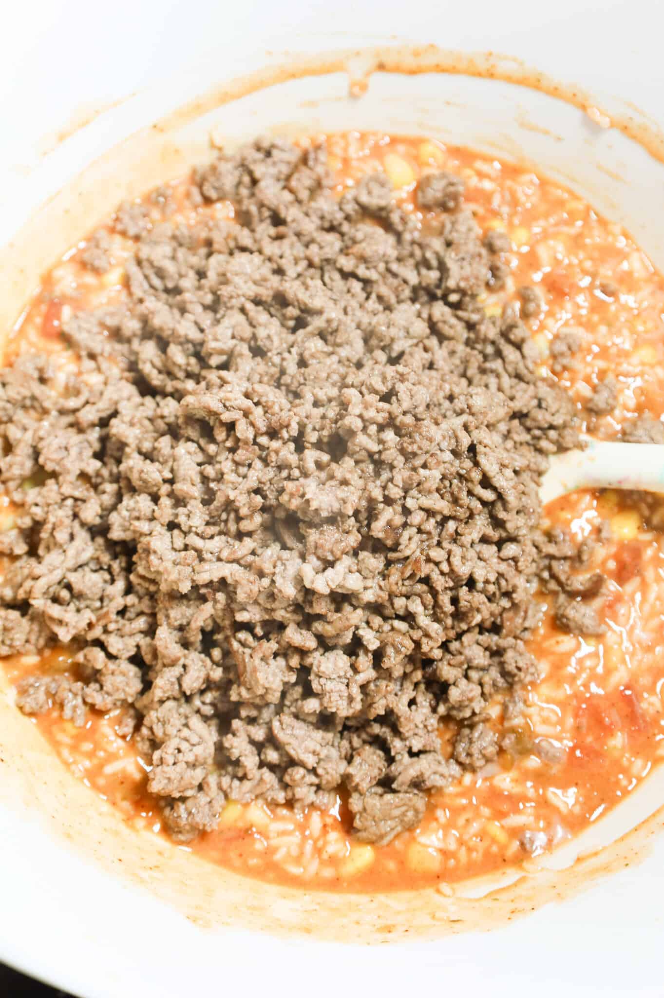 cooked ground beef on top of salsa and rice mixture in a mixing bowl