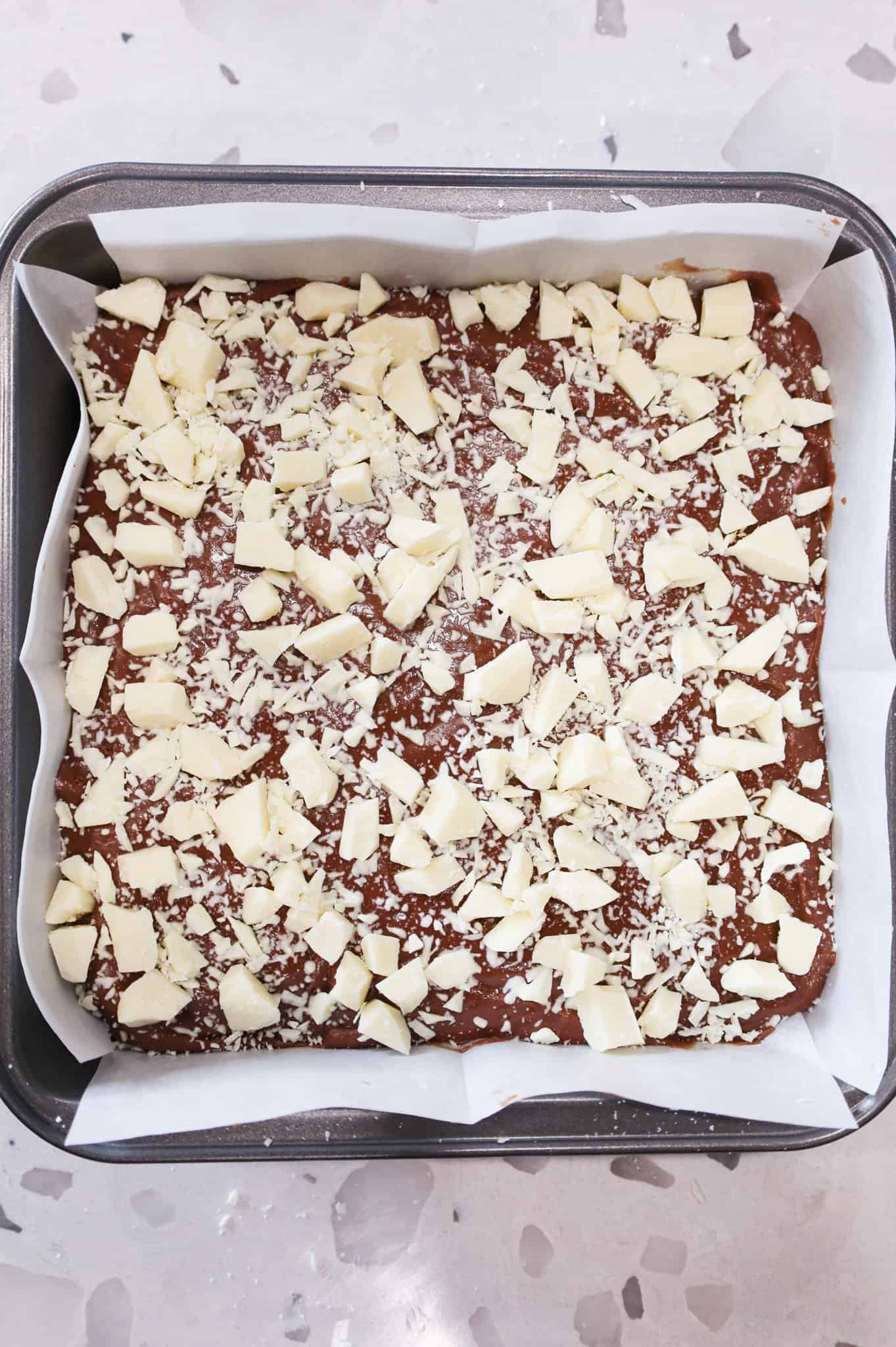 chopped white chocolate on top of fudge in a pan