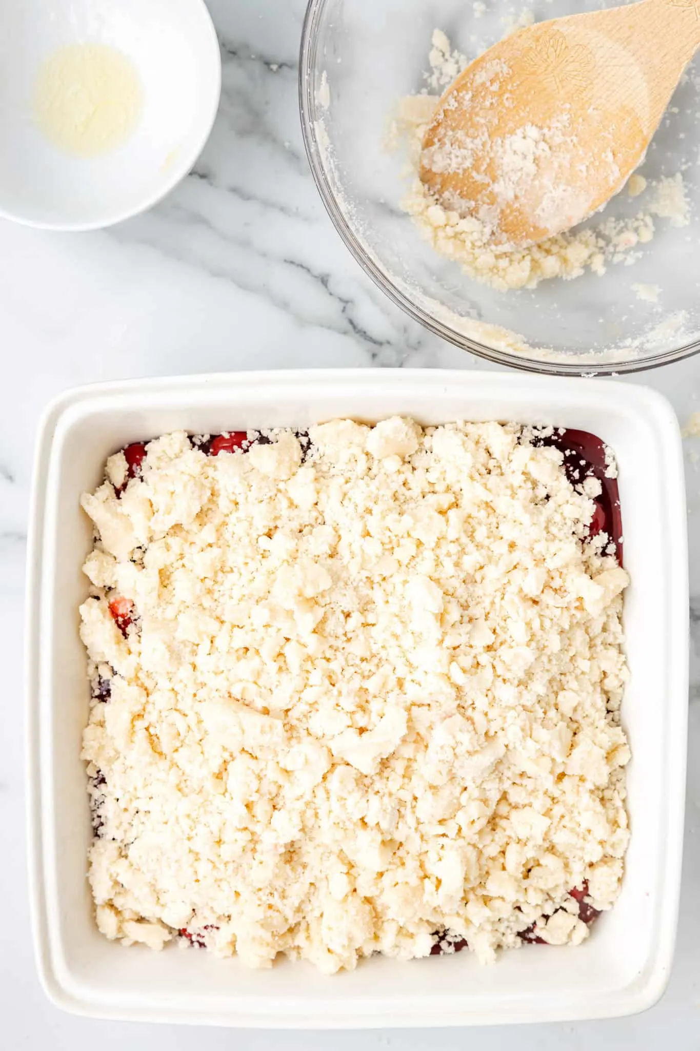 sugar cookie dough crumble on top of canned cherry pie filling in a baking dish