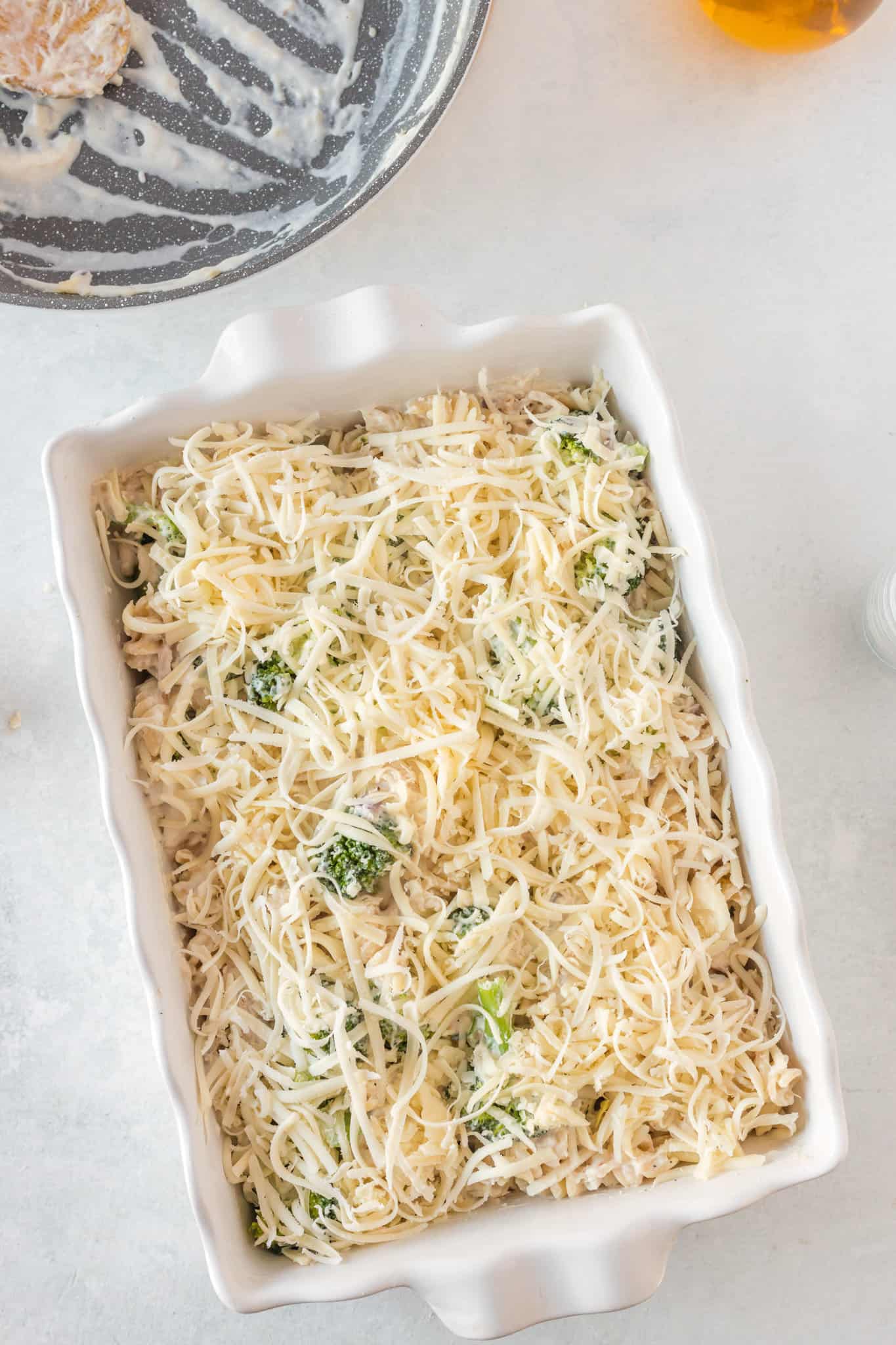 shredded cheddar cheese on top of chicken, broccoli and pasta mixture in a baking dish