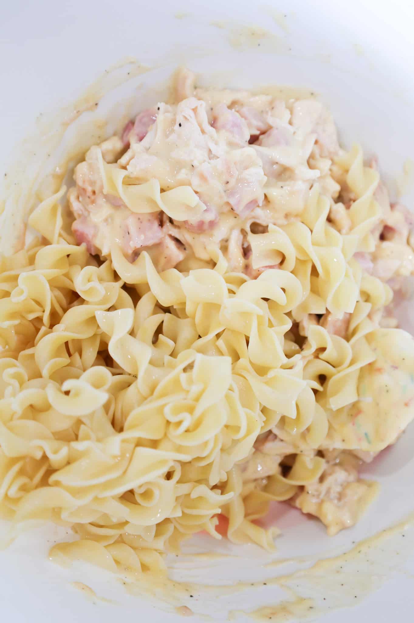 cooked egg noodles on top of chicken, ham and cream of chicken mixture in a mixing bowl
