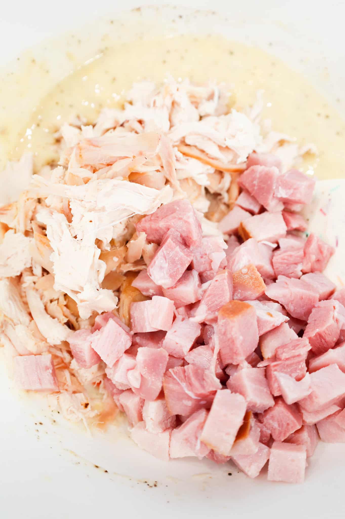 chopped ham and shredded chicken on top of cream of chicken soup in a mixing bowl