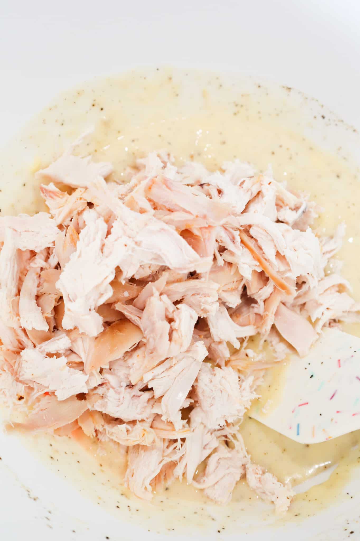 shredded chicken on top of cream of chicken mixture in a mixing bowl