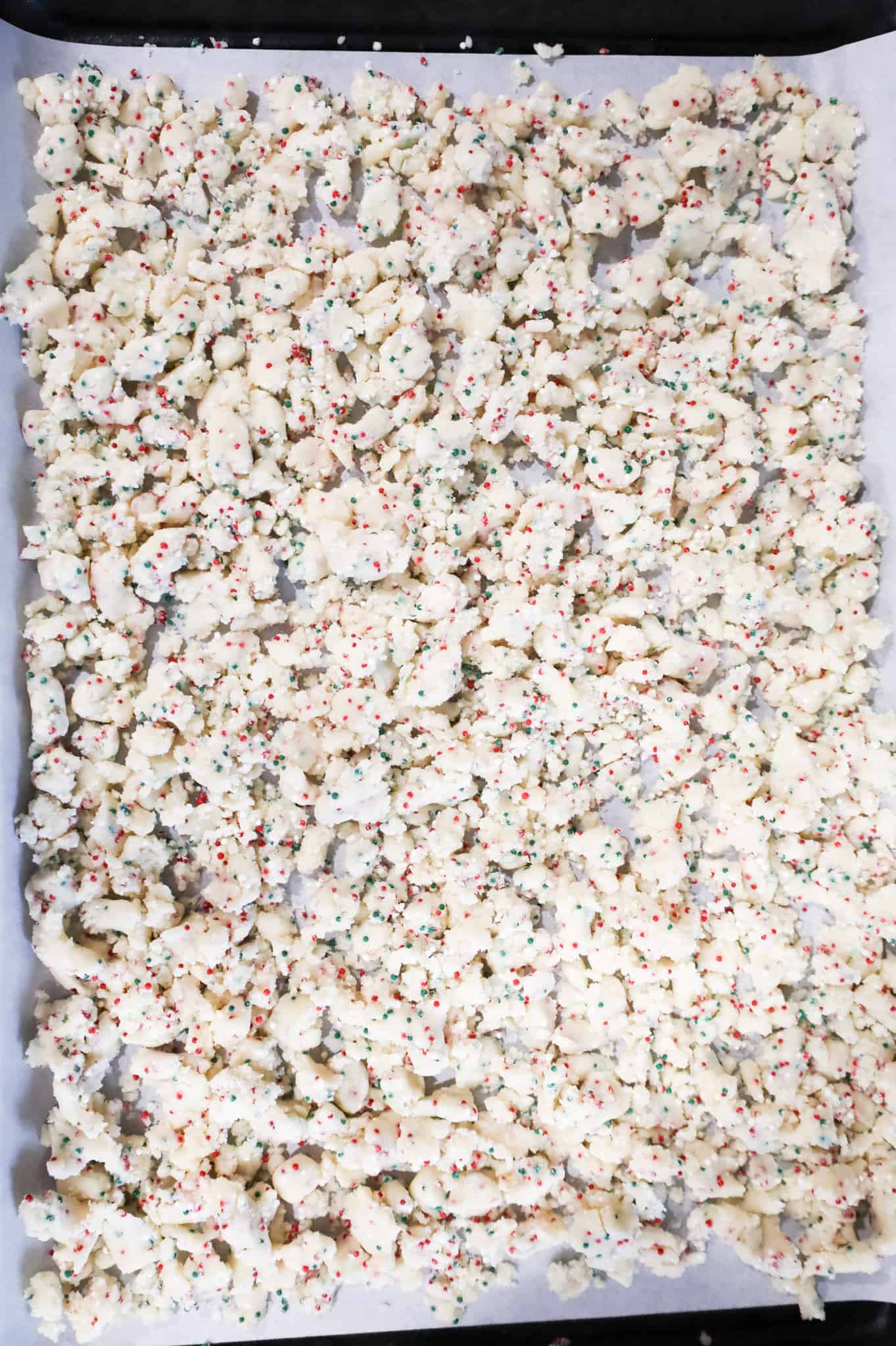 crumbled sugar cookie dough on a parchment lined baking sheet