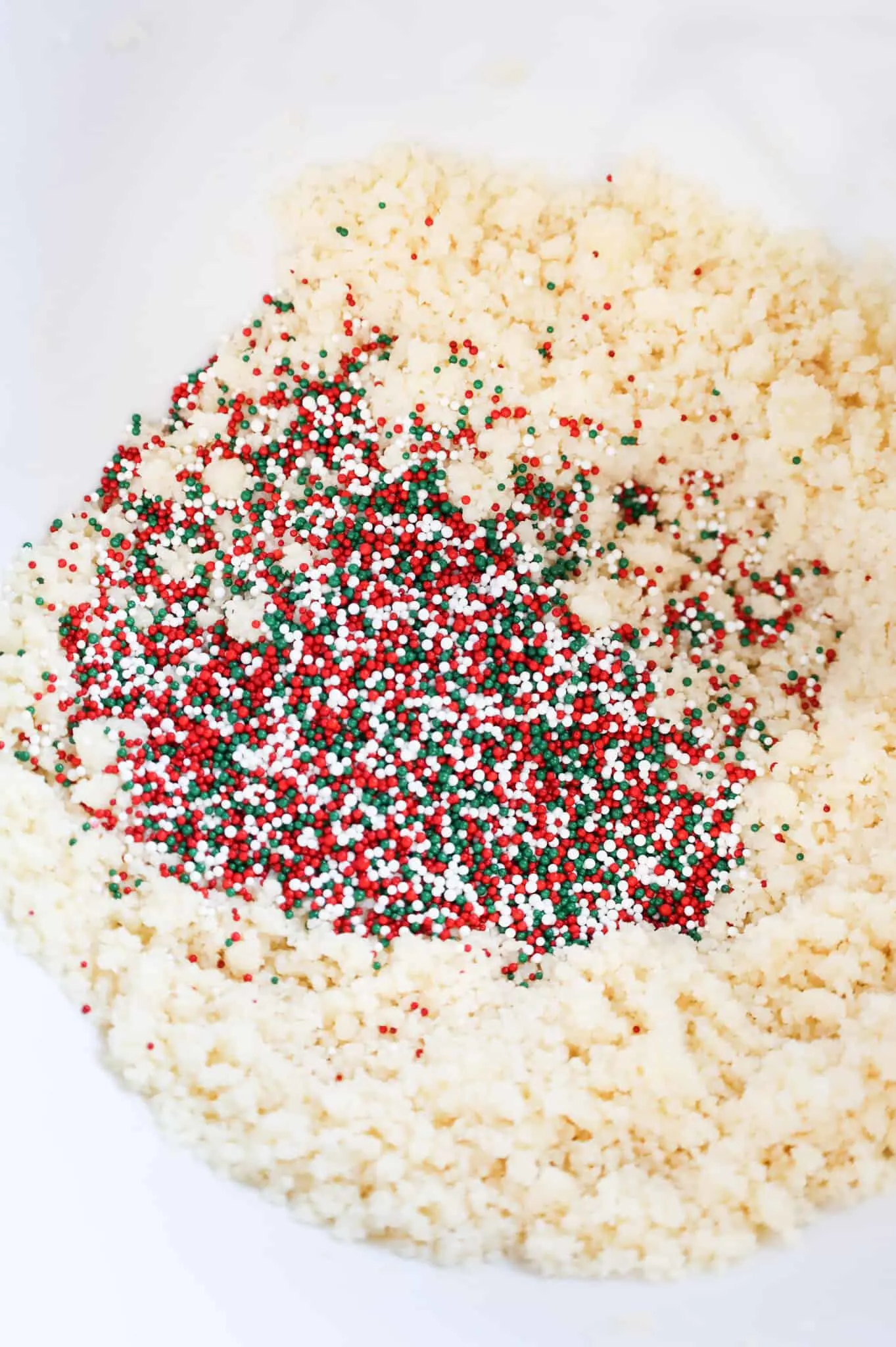 white, red, and green sprinkles added to bowl with sugar cookie dough