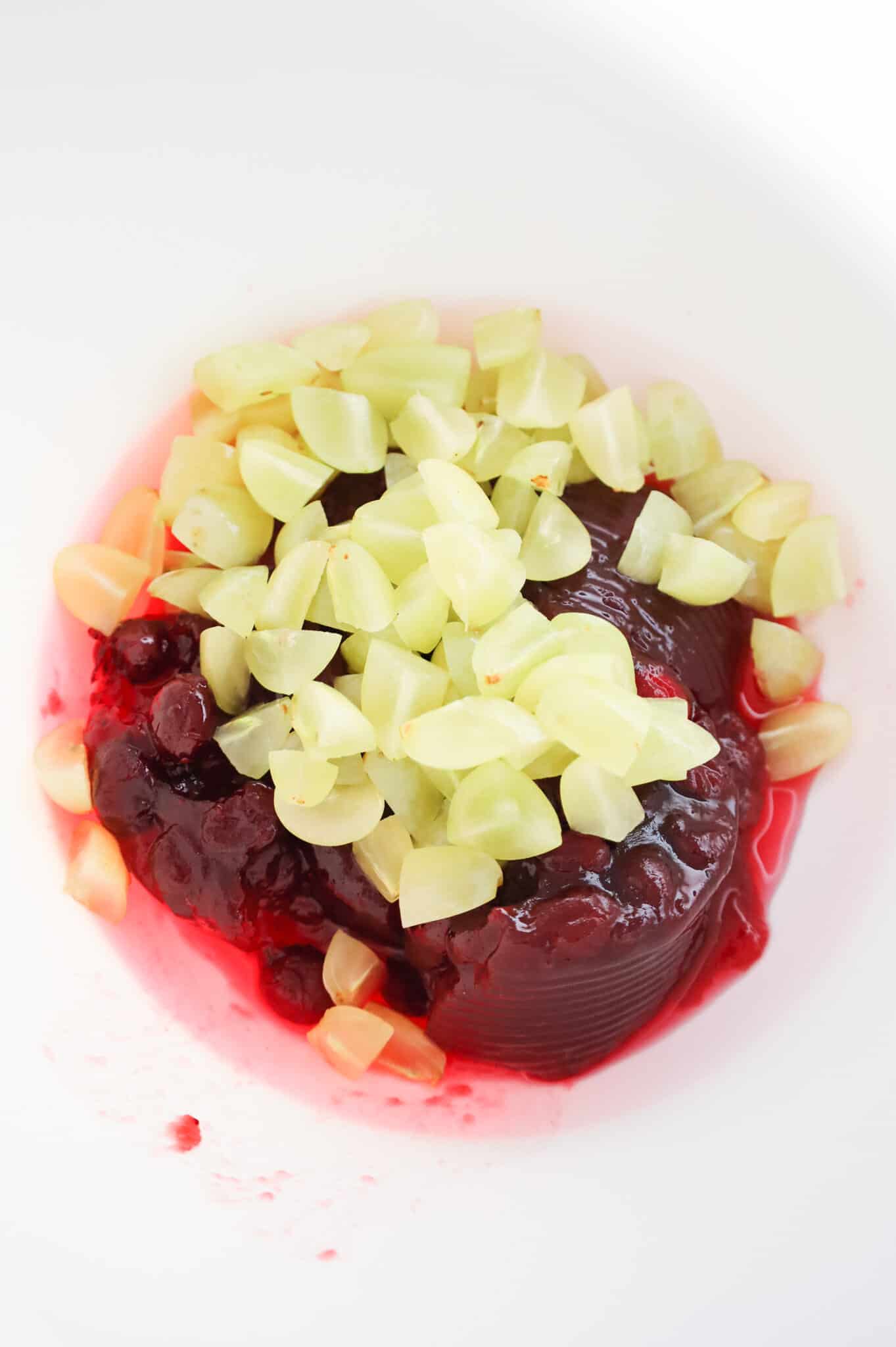 chopped green grapes and whole cranberry sauce in a mixing bowl