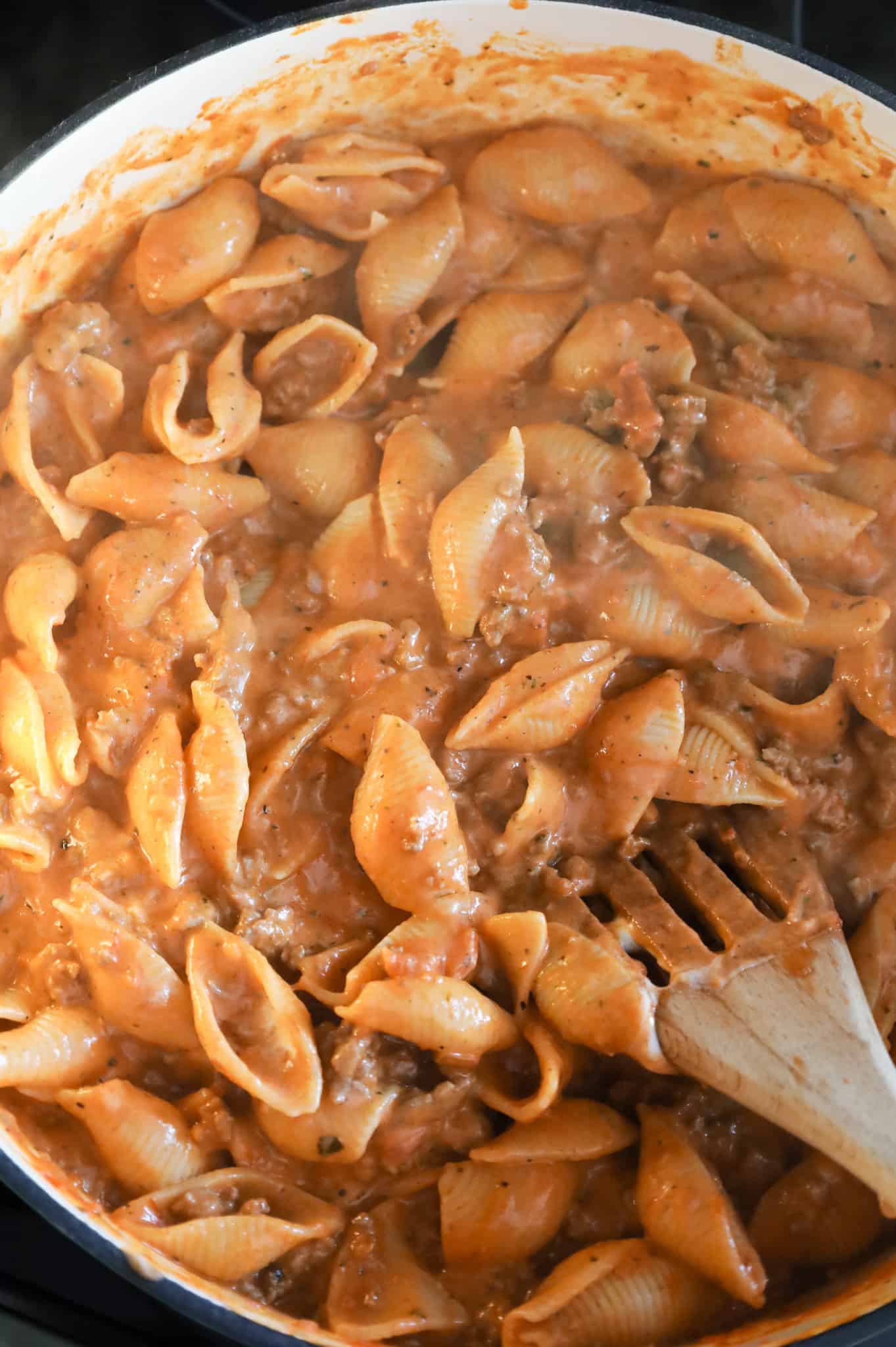 creamy ground beef and shells being stirred in a skillet