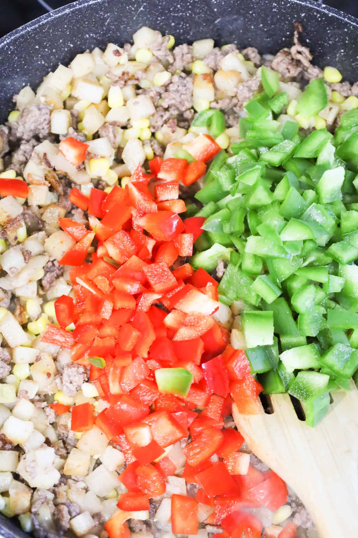 diced red and green peppers on top of ground beef and potato mixture in a skillet