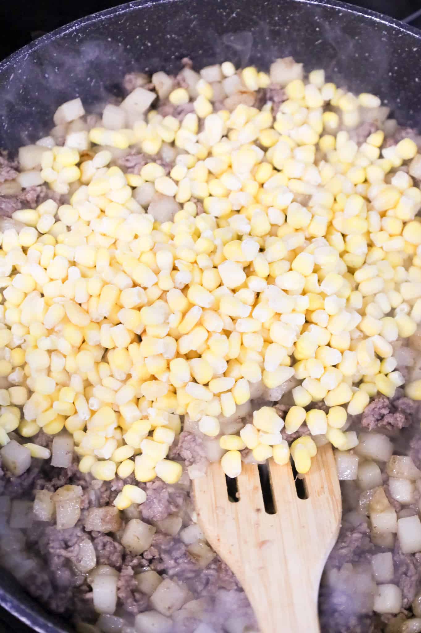 frozen corn kernels added to skillet with ground beef and diced potatoes