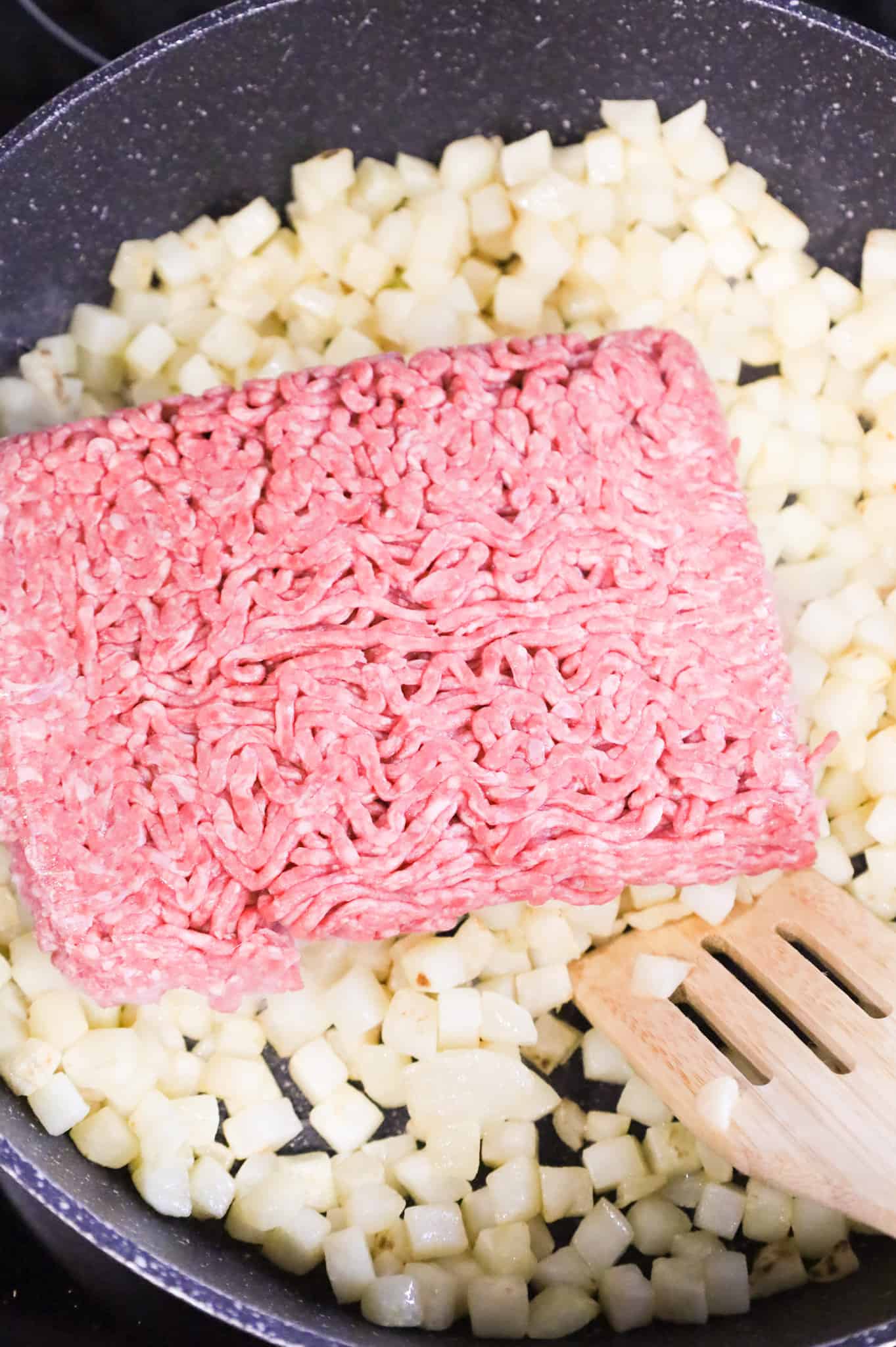 raw ground beef on top of diced potatoes in a skillet