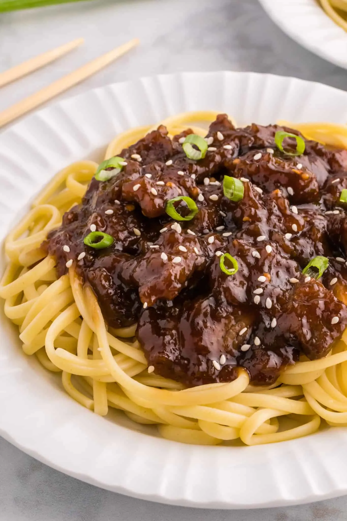 Mongolian Beef is a delicious dish with crispy fried steak strips cooked simmered in a brown sugar and soy sauce mixture served over noodles or rice and garnished with sesame seeds and green onions.