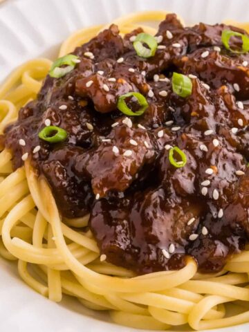 Mongolian Beef is a delicious dish with crispy fried steak strips cooked simmered in a brown sugar and soy sauce mixture served over noodles or rice and garnished with sesame seeds and green onions.