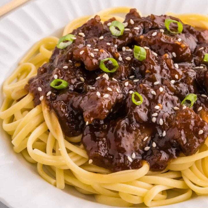 Mongolian Beef is a delicious dish with crispy fried steak strips cooked simmered in a brown sugar and soy sauce mixture served over noodles or rice and garnished with sesame seeds and green onions.