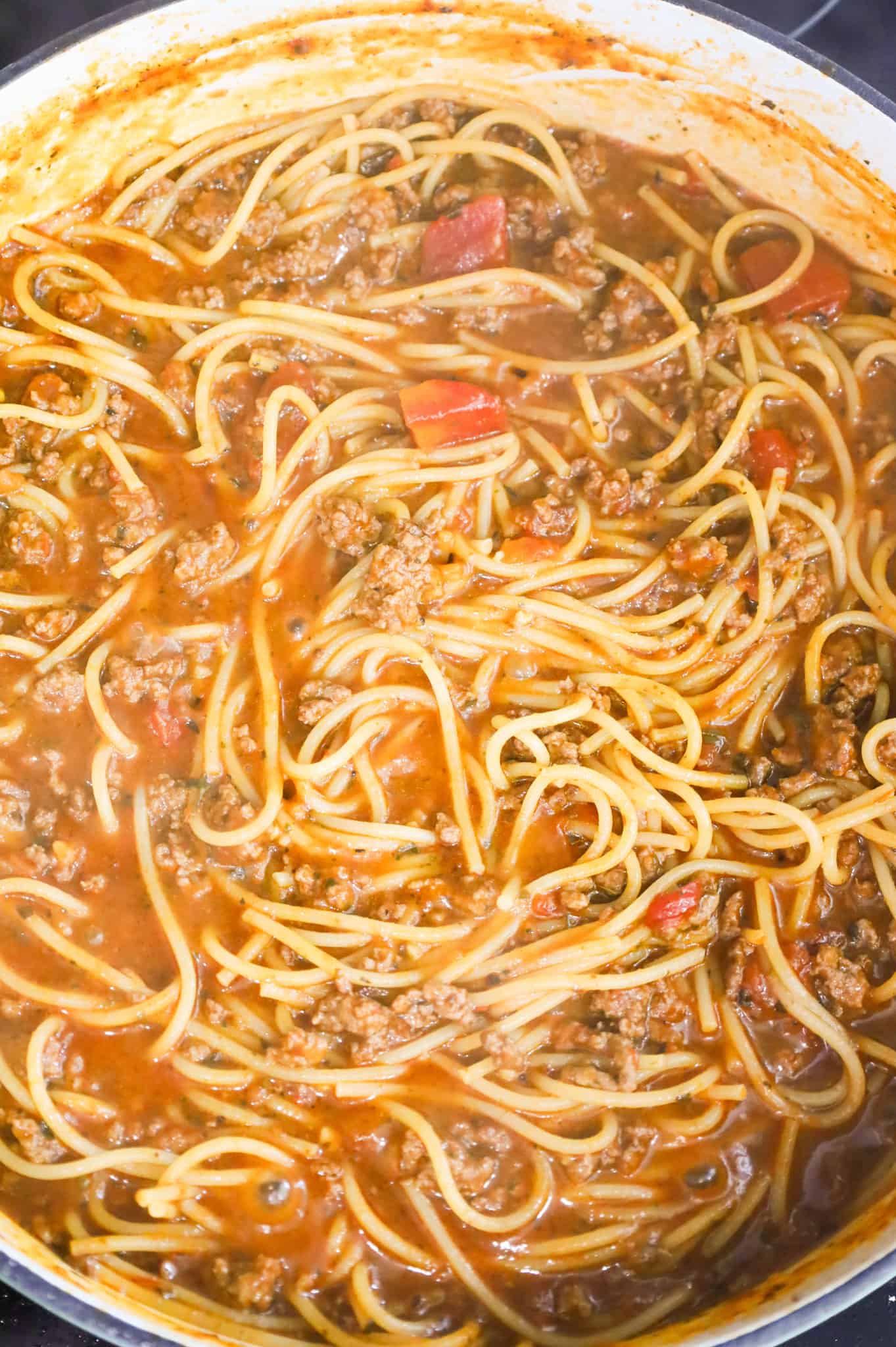 spaghetti noodles cooking in marinara and beef broth mixture in a skillet