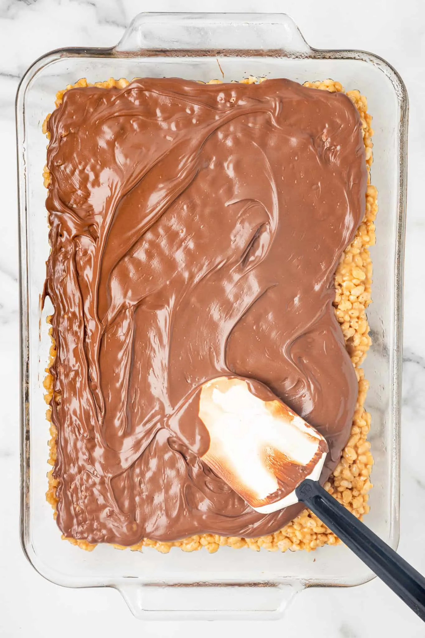 spreading melted chocolate and butterscotch mixture over peanut butter rice krispies in a baking dish