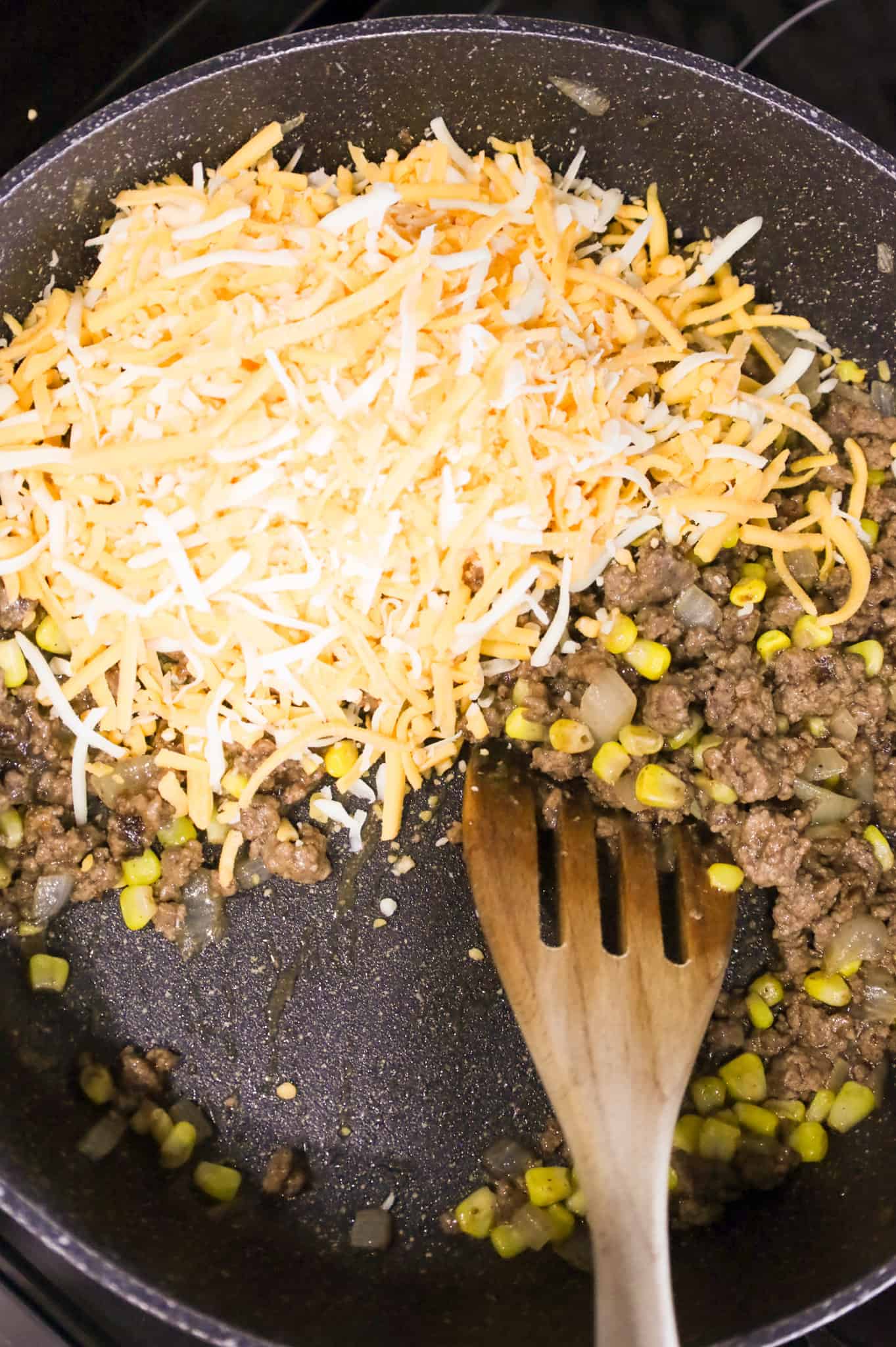 shredded cheese on top of ground beef mixture in a skillet