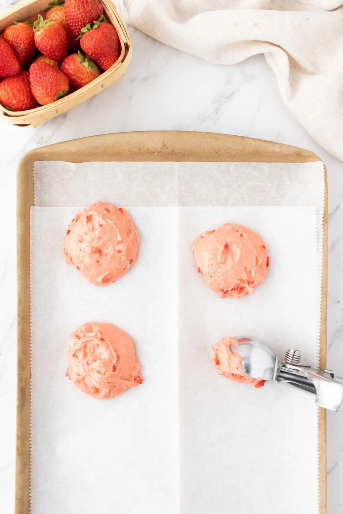strawberry cookie dough being scooped onto parchment lined baking sheet