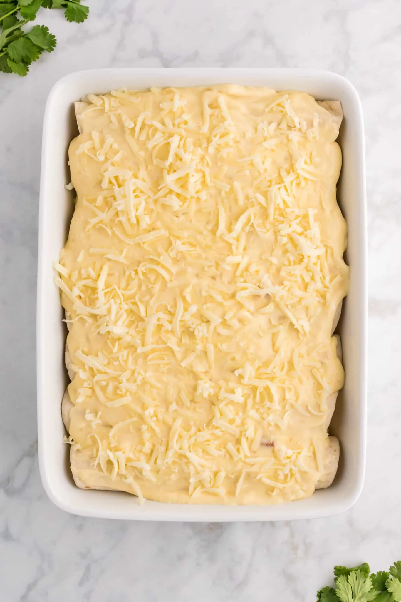 shredded cheese and cream sauce on top of enchiladas in a baking dish