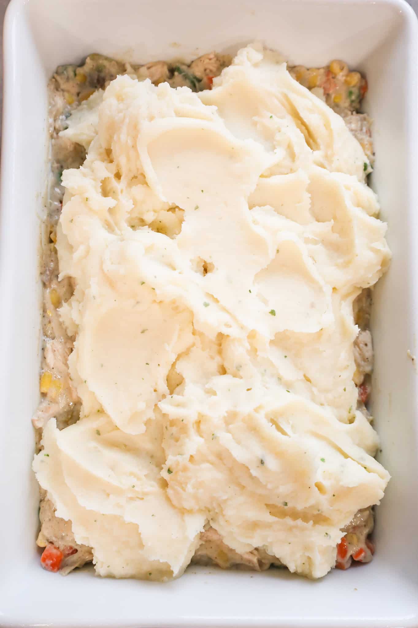 mashed potatoes scooped on top of chicken mixture in a baking dish