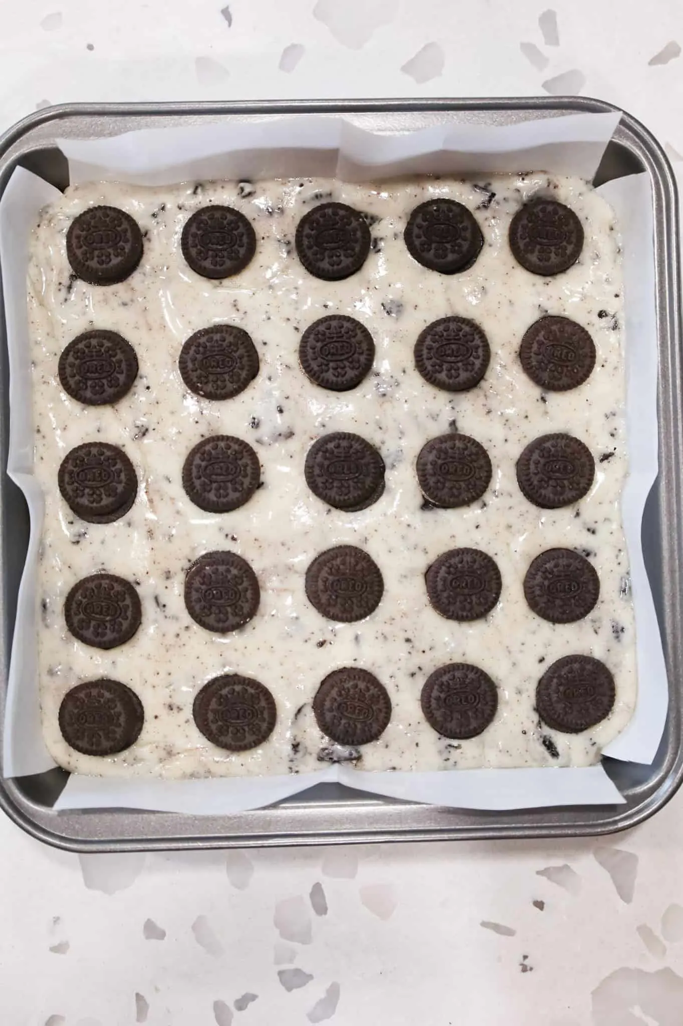 mini Oreos on top of Oreo fudge in a parchment lined baking pan