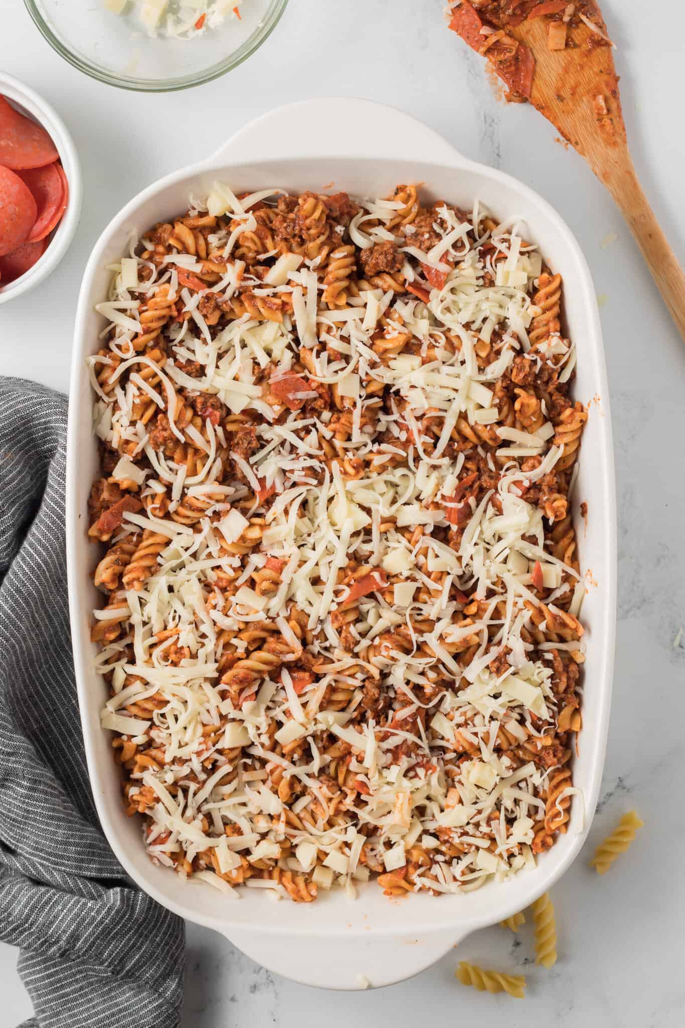 shredded mozzarella cheese on top of pizza pasta in a baking dish
