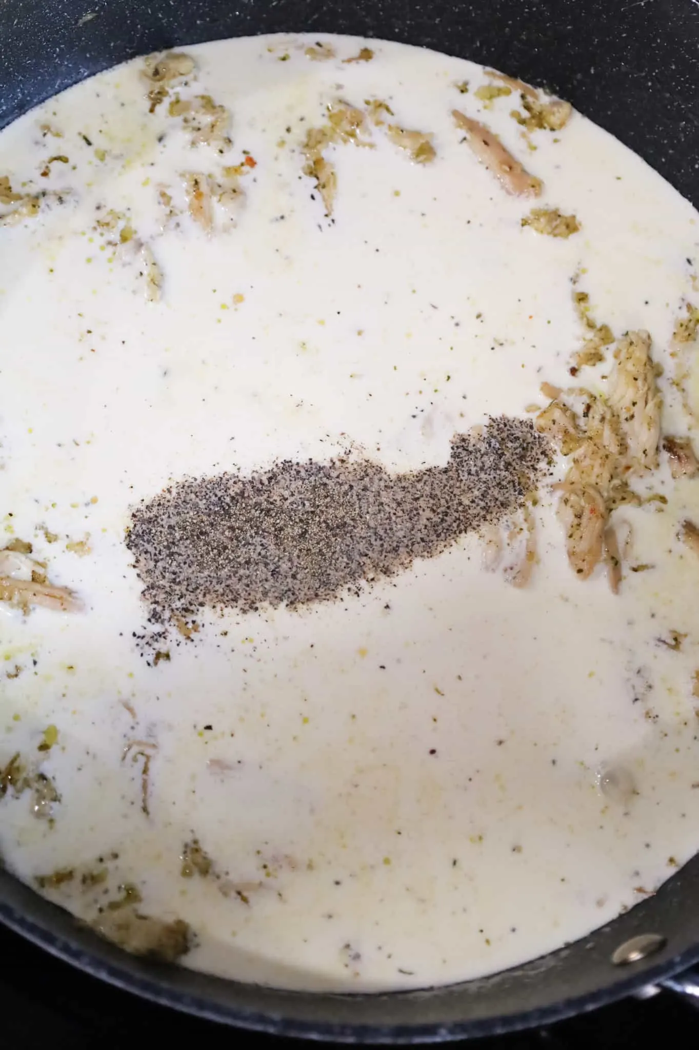 salt, pepper and heavy cream added to a skillet with shredded chicken
