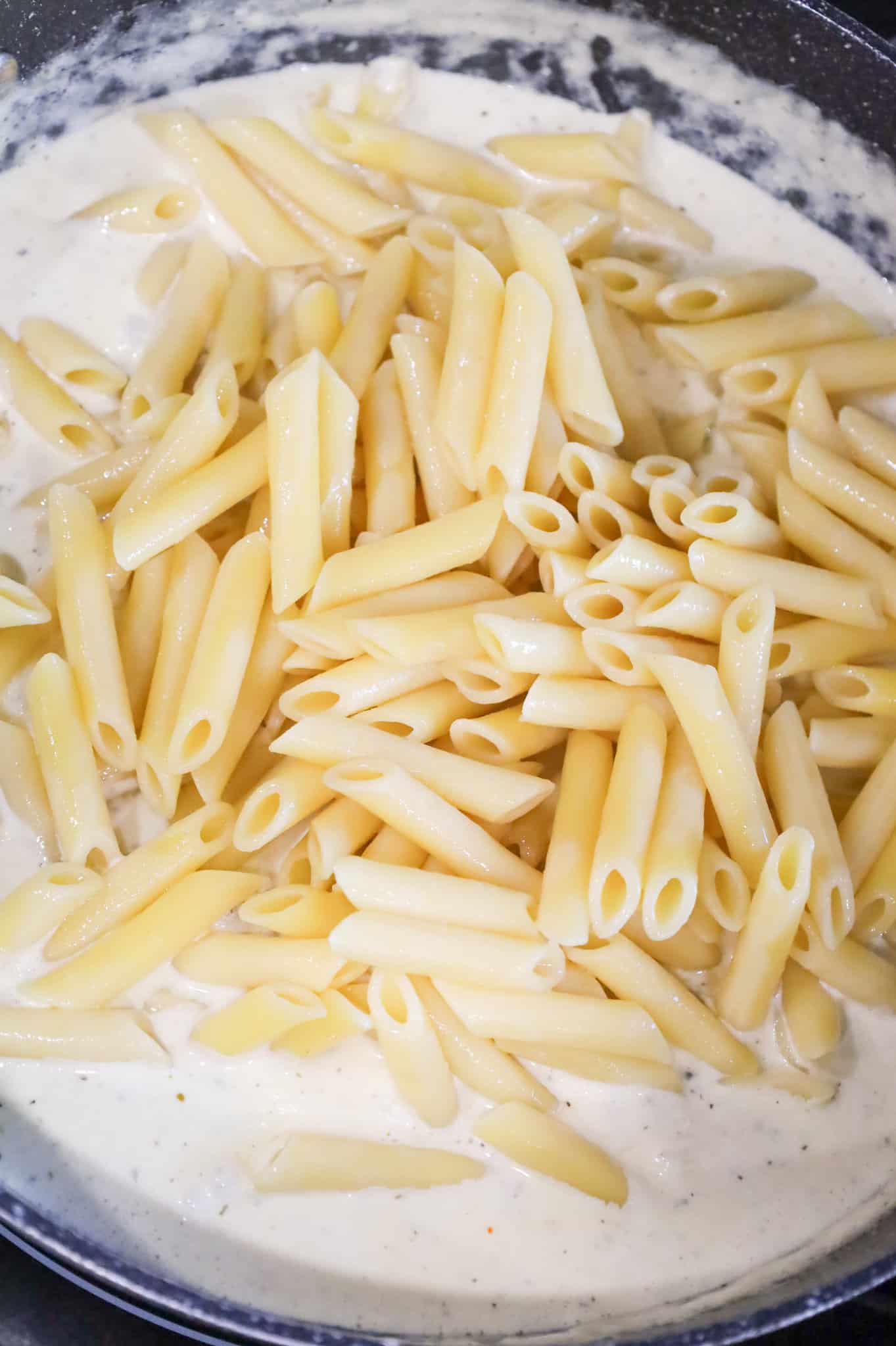 cooked penne noodles added to skillet with cream sauce