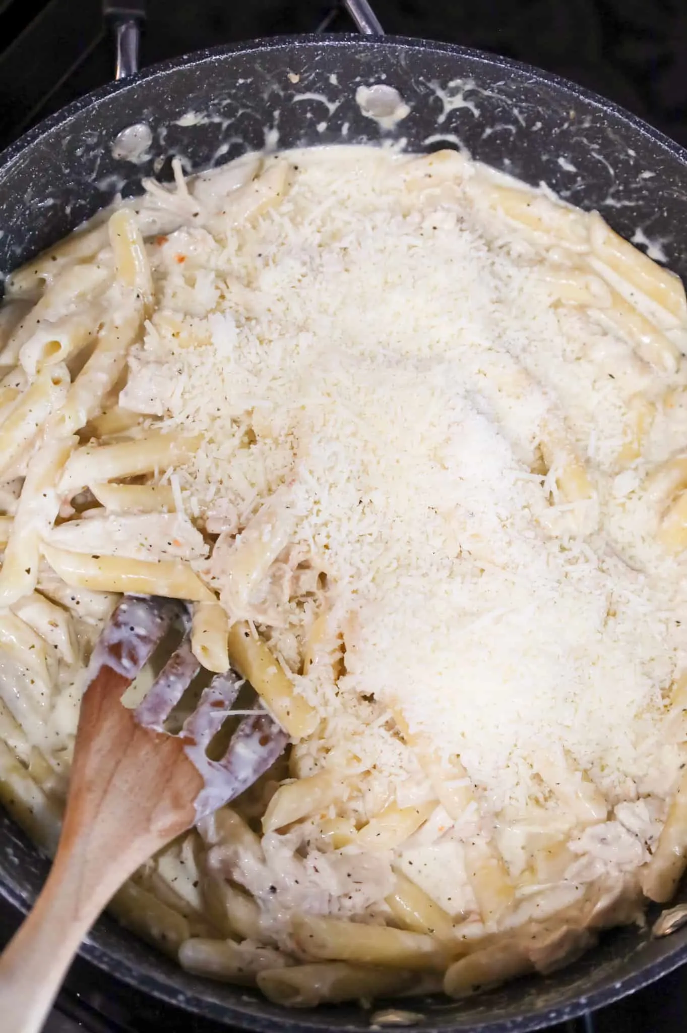 shredded parmesan cheese on top of creamy penne pasta in a skillet