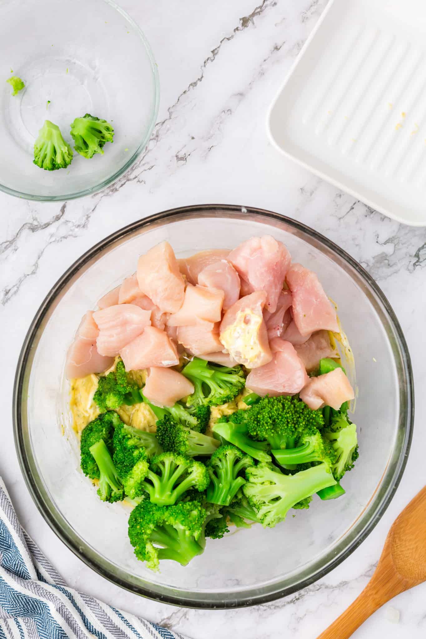 raw chicken breast chunks and broccoli florets on top broccoli soup and cheese mixture in a mixing bowl