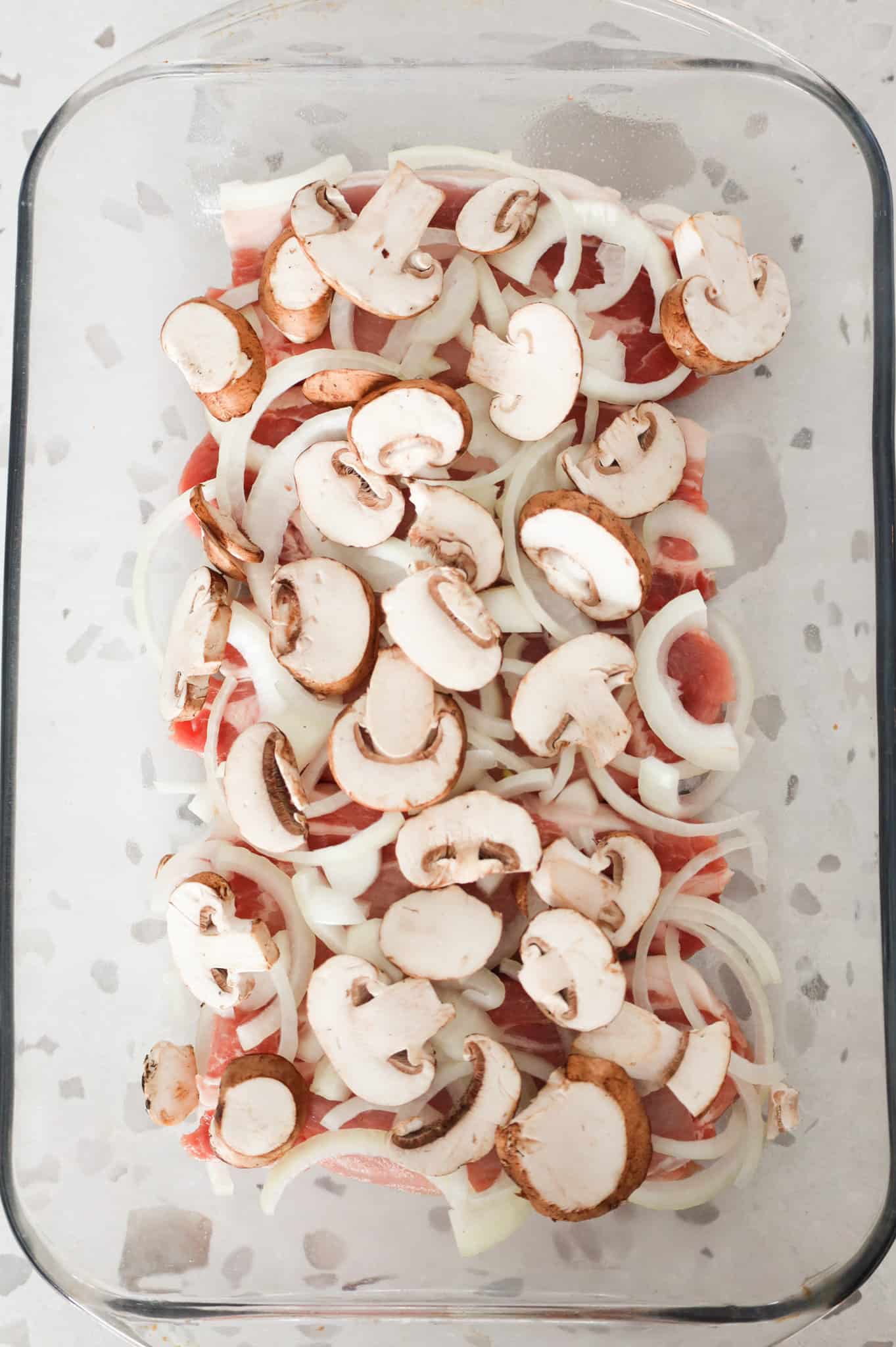 sliced mushrooms and onions on top of pork chops in a baking dish