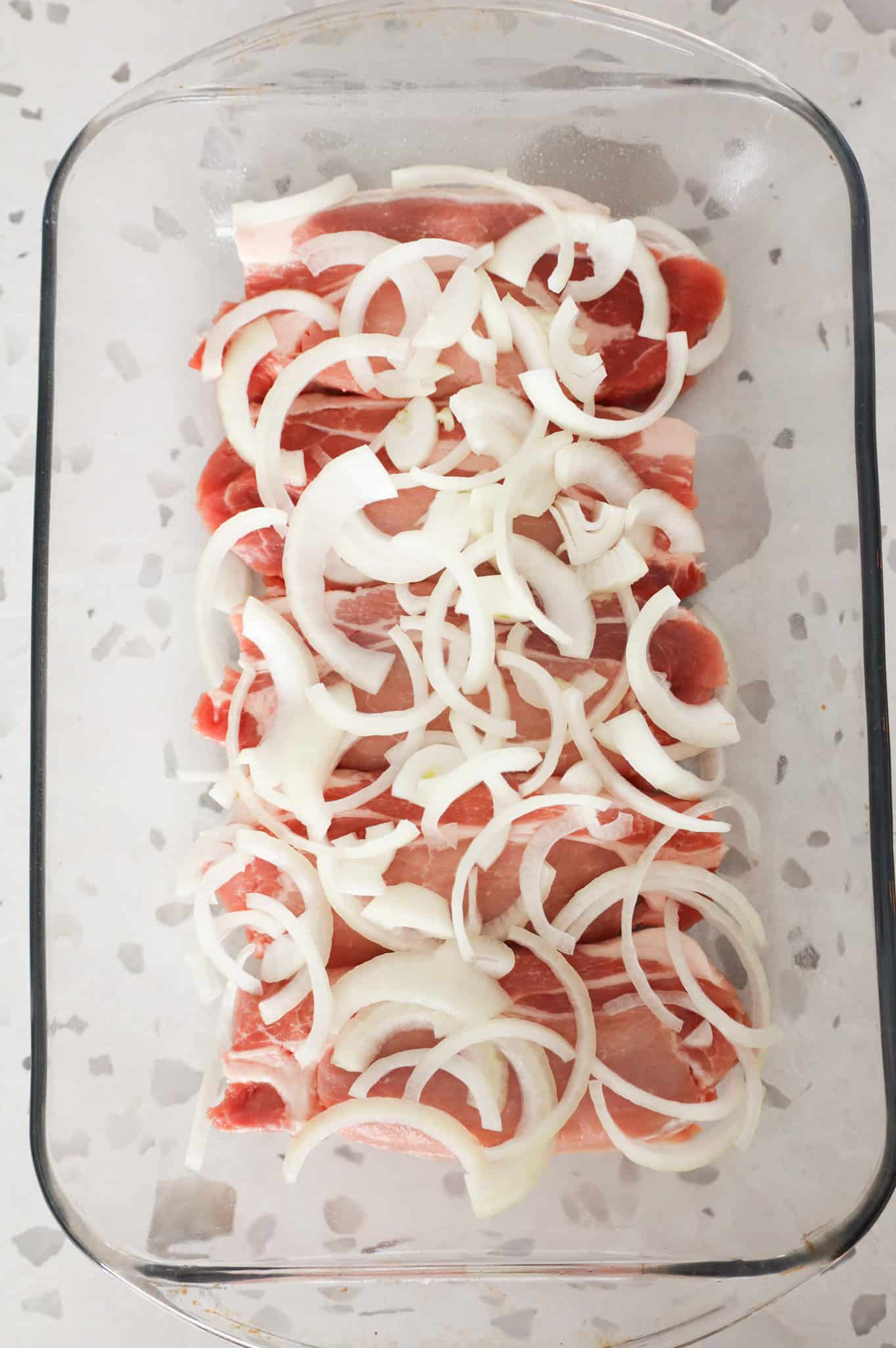sliced onions on top of pork chops in a baking dish