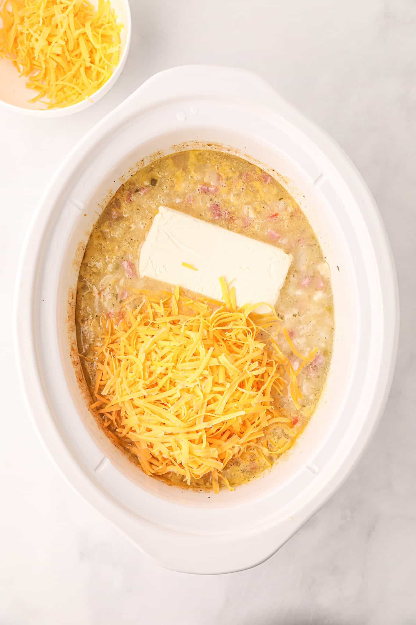 cream cheese and shredded cheddar cheese added to crock pot with potato soup