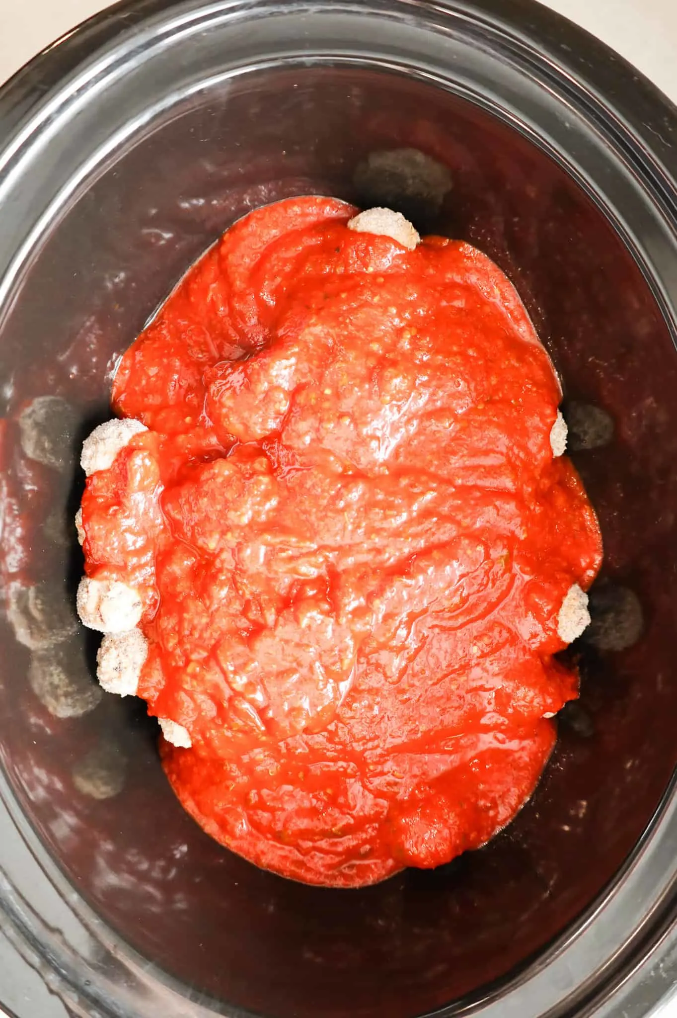 marinara sauce poured over frozen meatballs in a crock pot