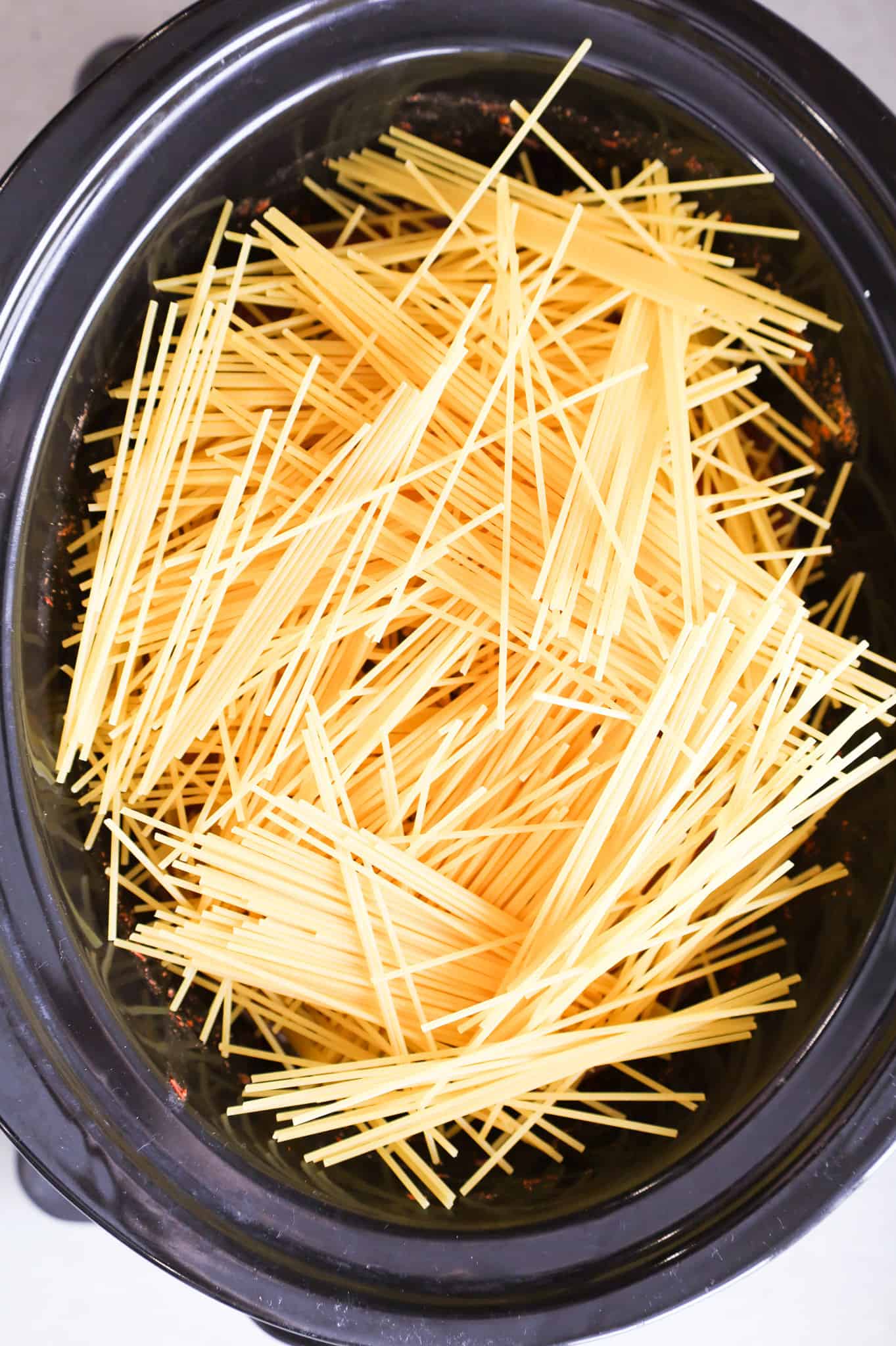 broken spaghetti noodles on top of meatballs and marinara in a crock pot