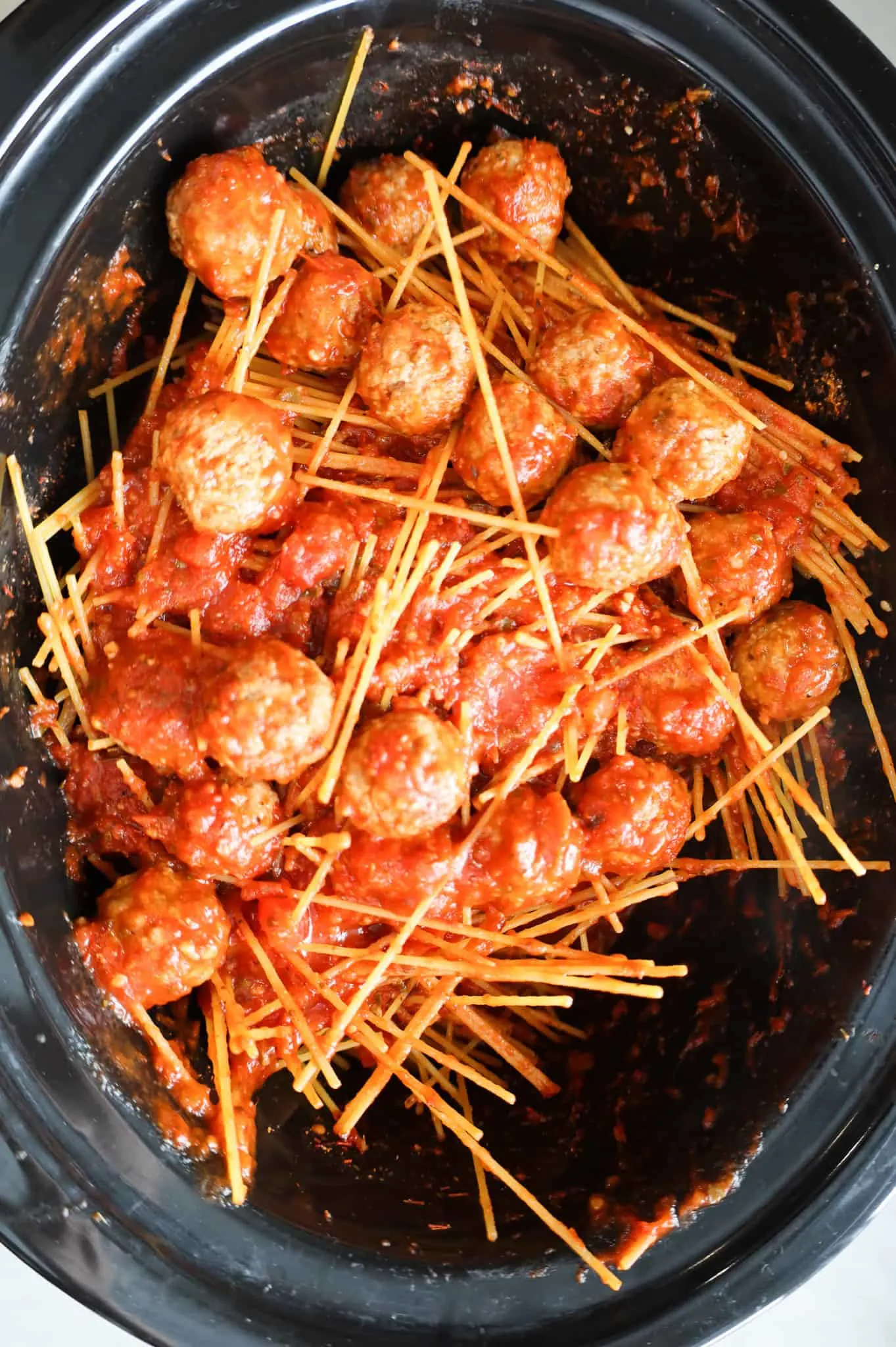 stirring together spaghetti noodles, meatballs and marinara sauce in a Crock pot