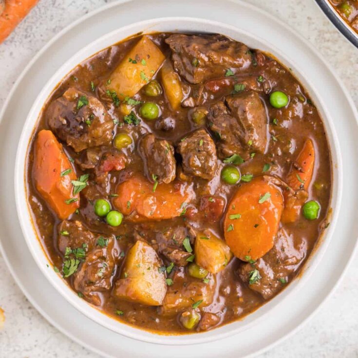 Dutch Oven Beef Stew is a hearty dish loaded with chunks of beef, carrots, onions, potatoes, tomatoes and peas.