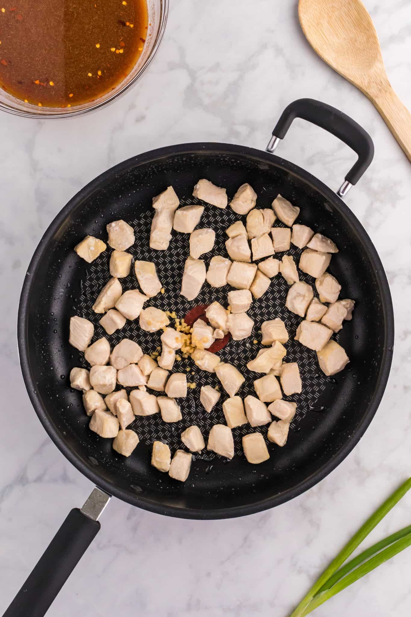 chicken chunks cooking in a skillet with garlic