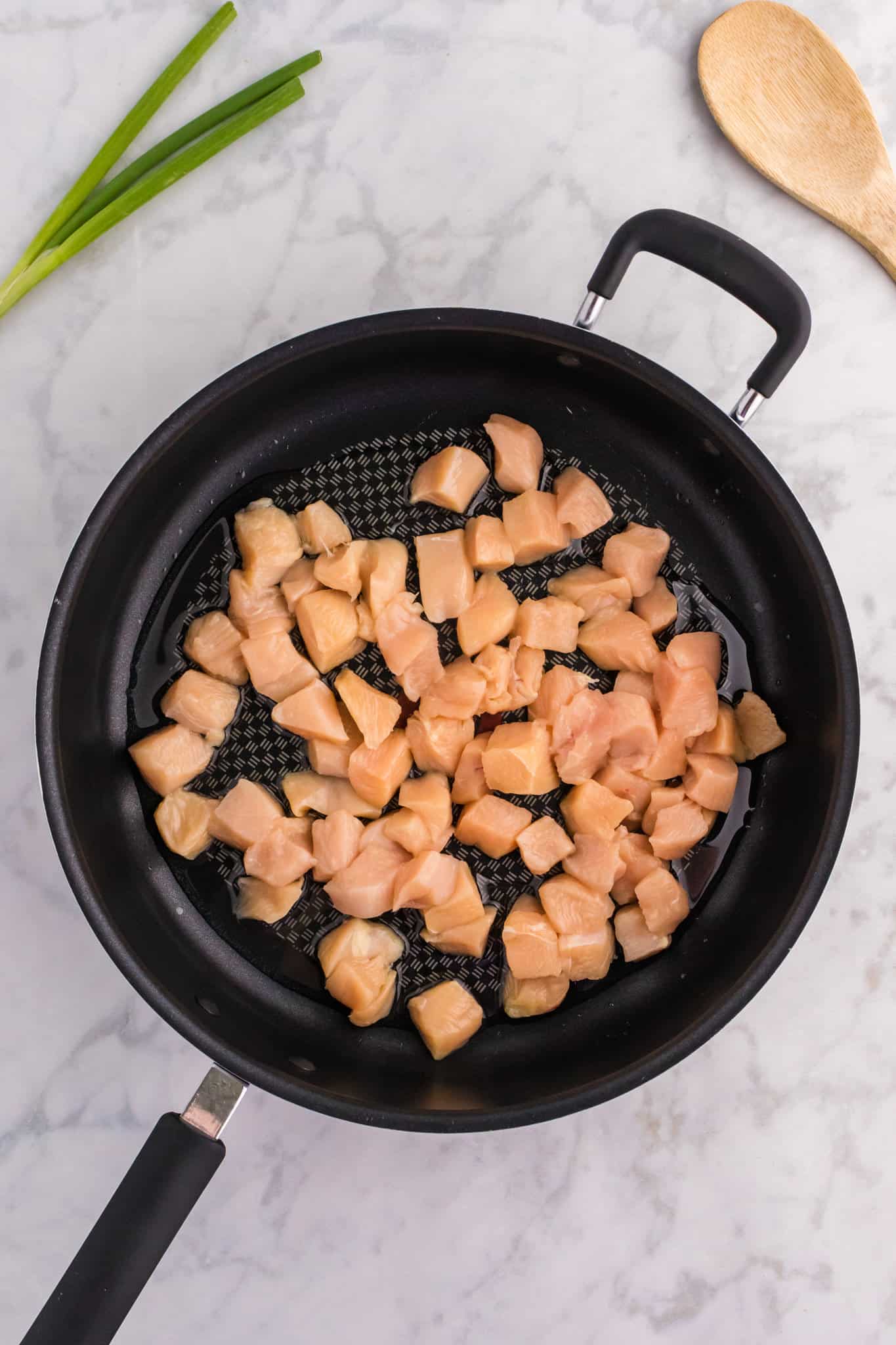 raw chicken breast chunks added to a skillet with hot oil