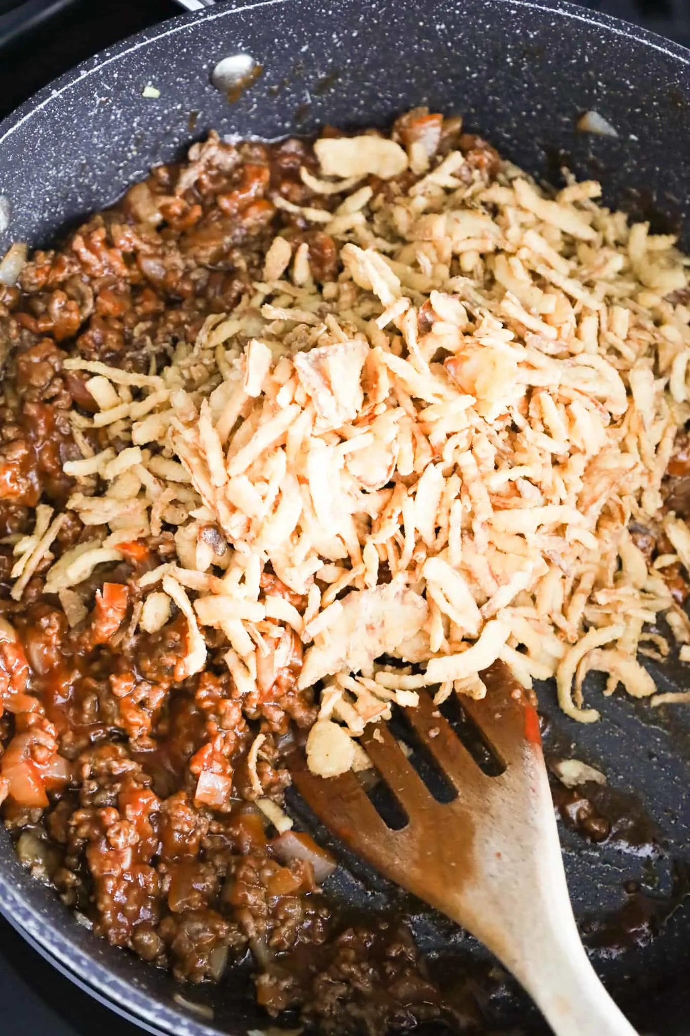 crispy fried onions added to skillet with cooked ground beef in a sloppy joe sauce