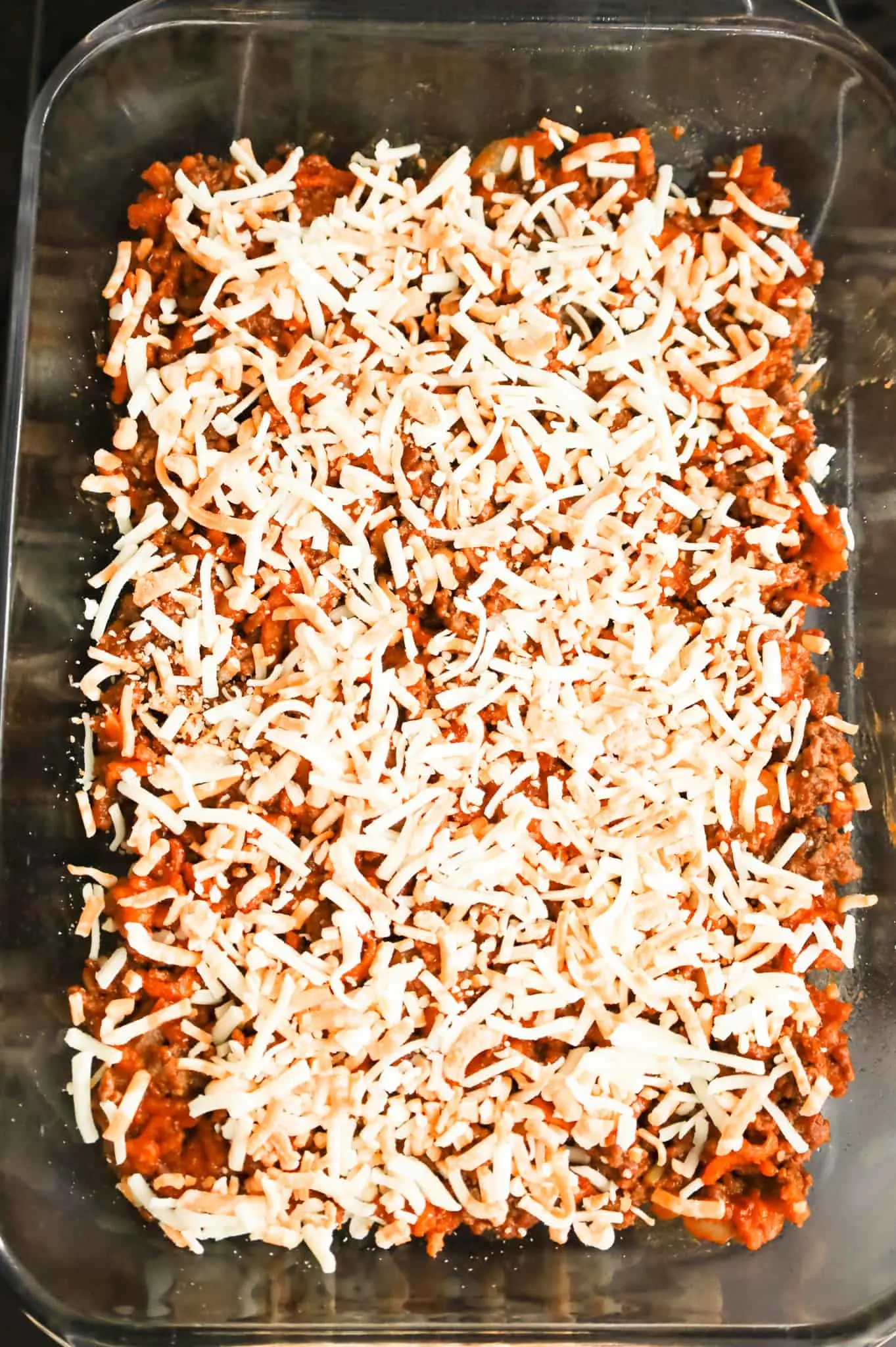 shredded cheese on top of ground beef sloppy joe mixture in a baking dish