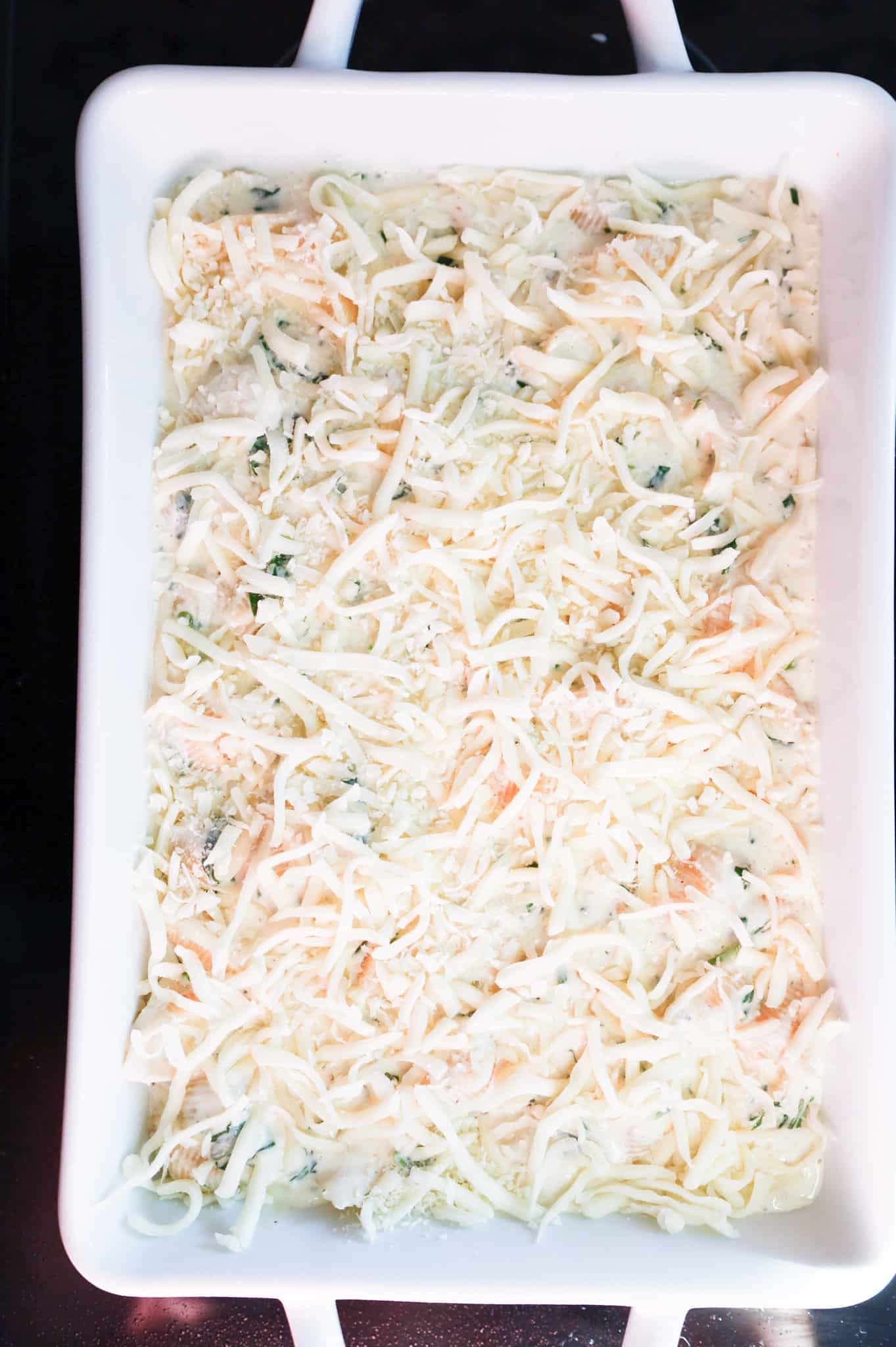 shredded mozzarella cheese on top of creamy pasta in a baking dish